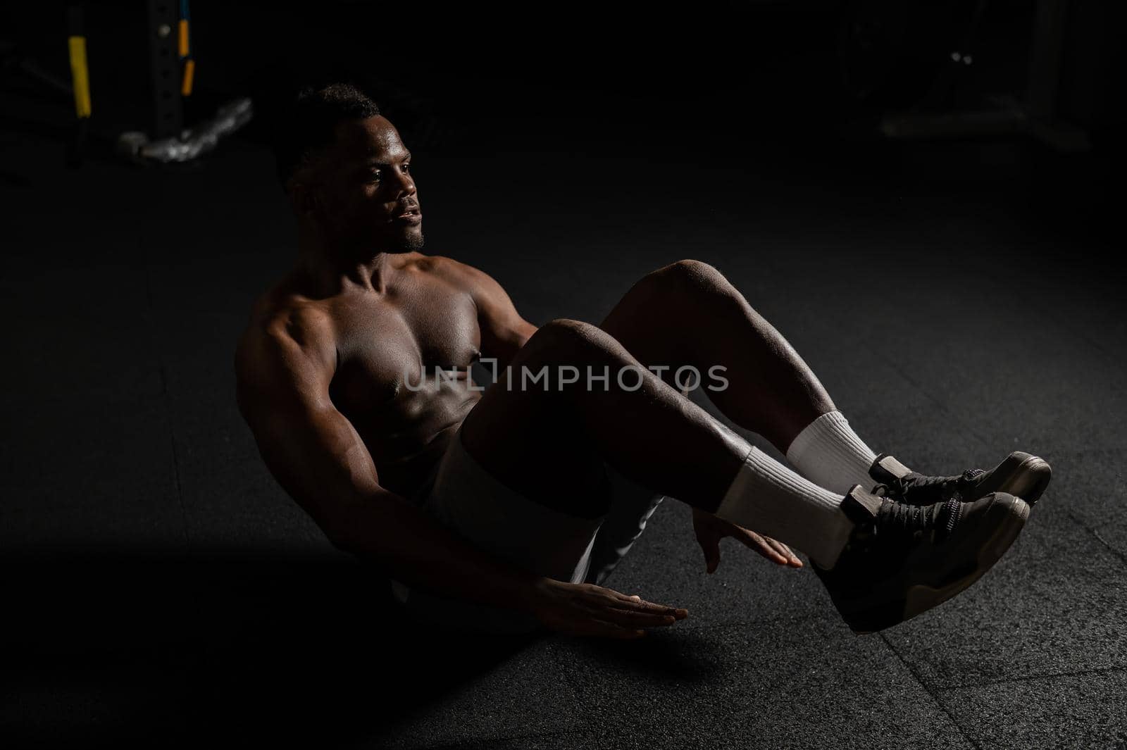 Afro american man doing abdominal exercises in a dark studio. by mrwed54