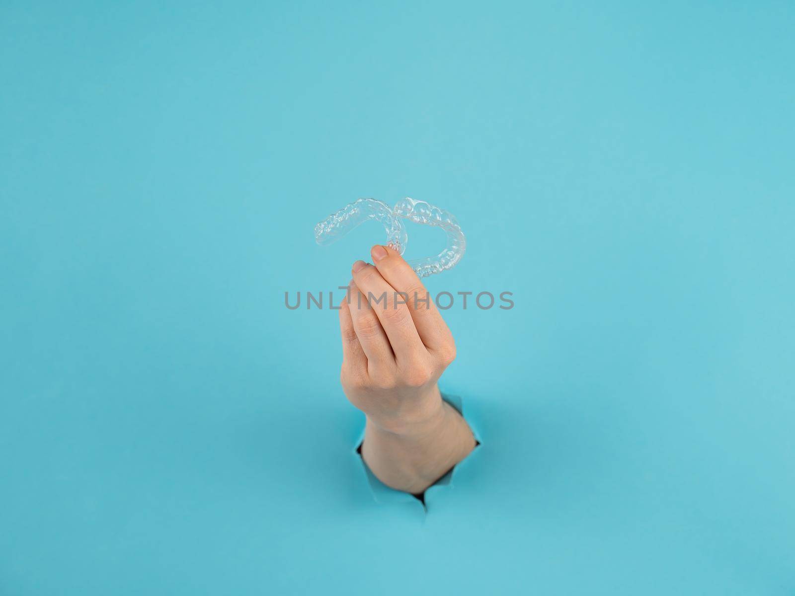 A female hand sticking out of a hole from a blue background holds removable night retainers. by mrwed54