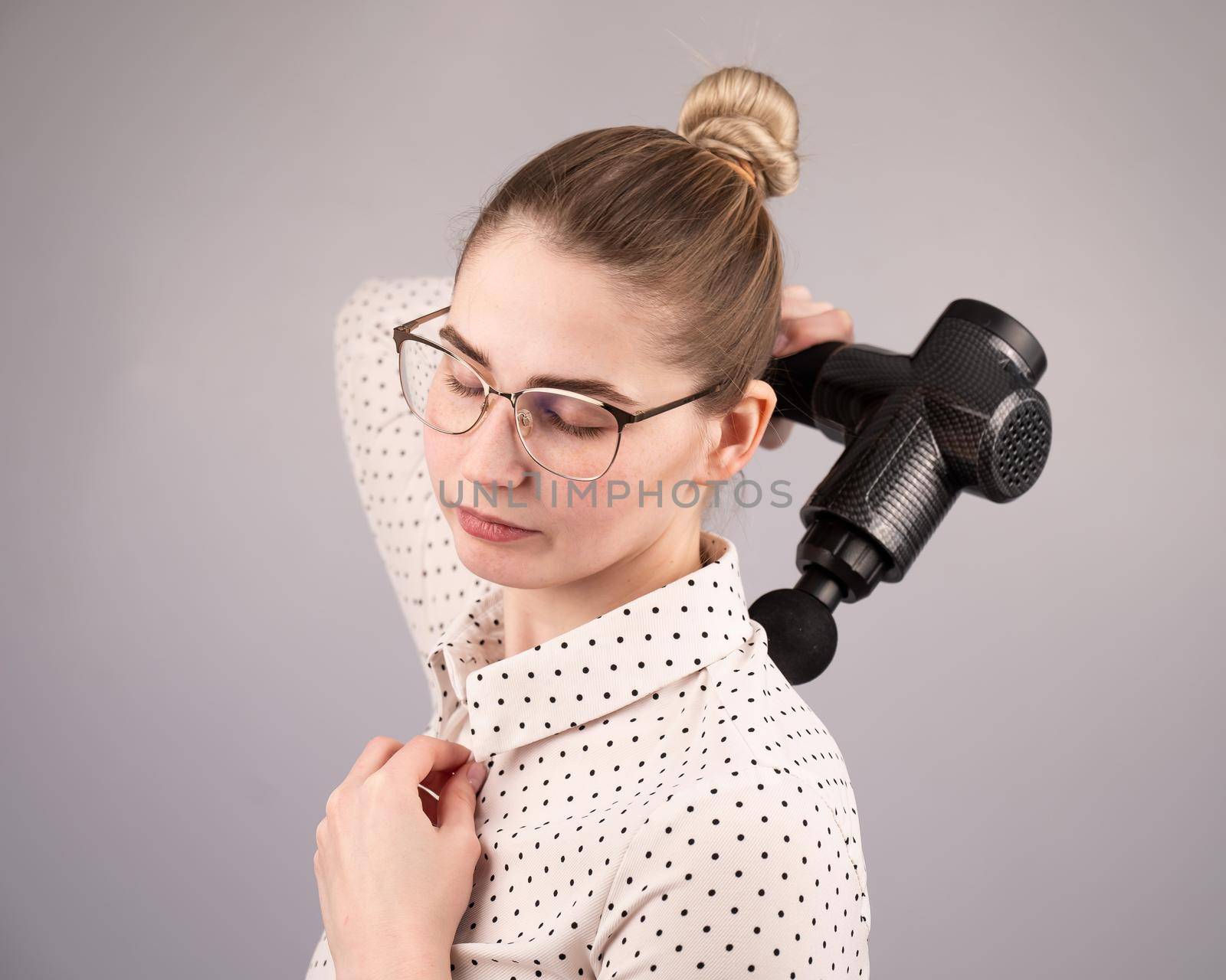 Caucasian business lady makes herself a back massage with a massager gun on a white background