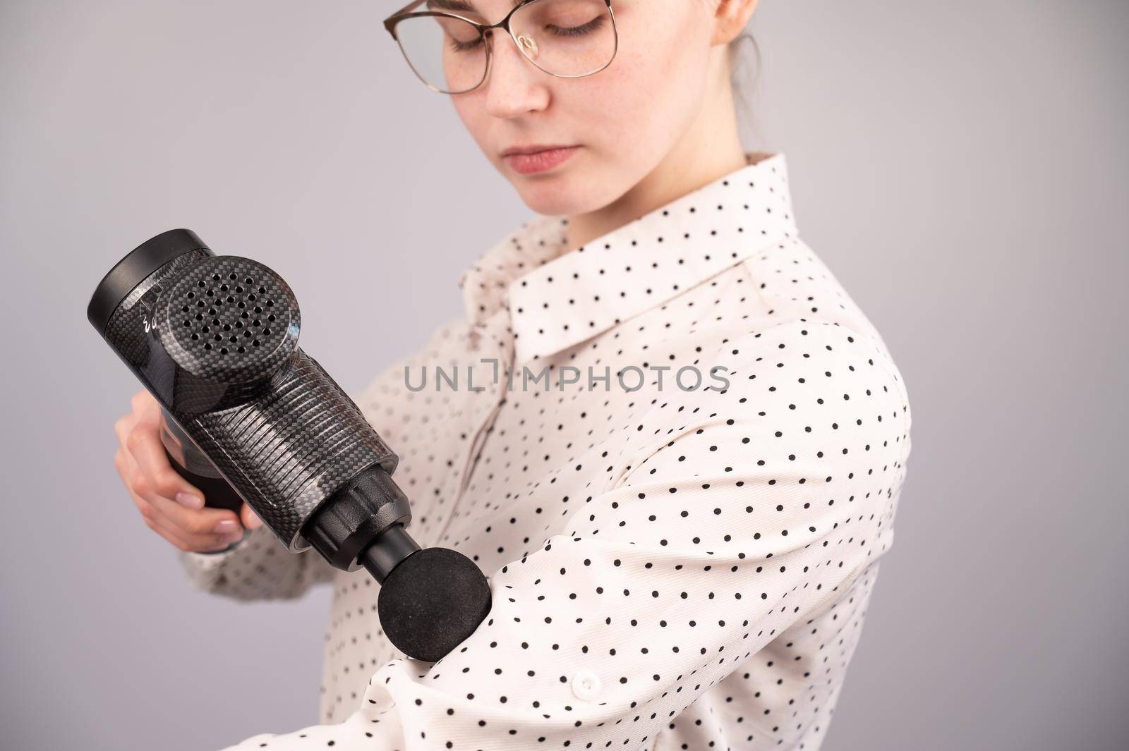 Caucasian business woman massaging her biceps with a percussion massager