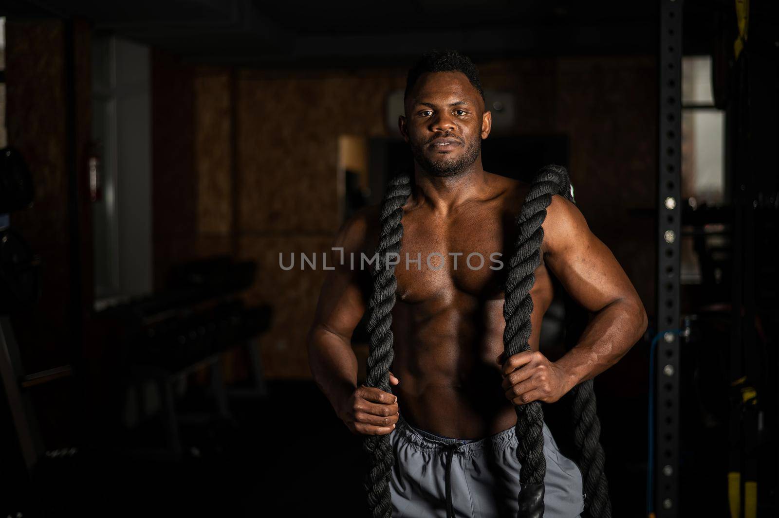 Muscular african american man posing with rope in gym. by mrwed54