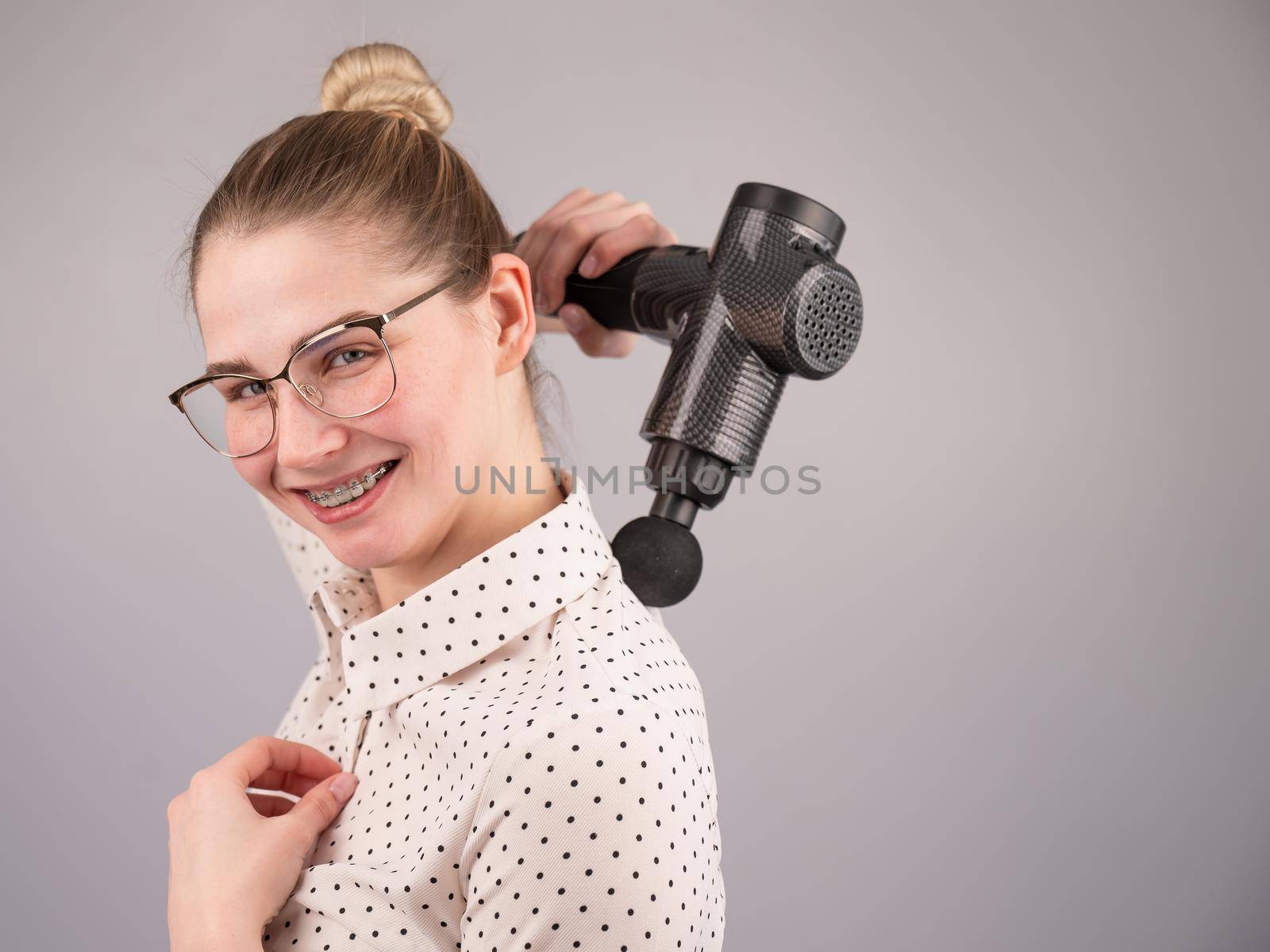 Smiling woman with braces uses a massager gun for her back. by mrwed54