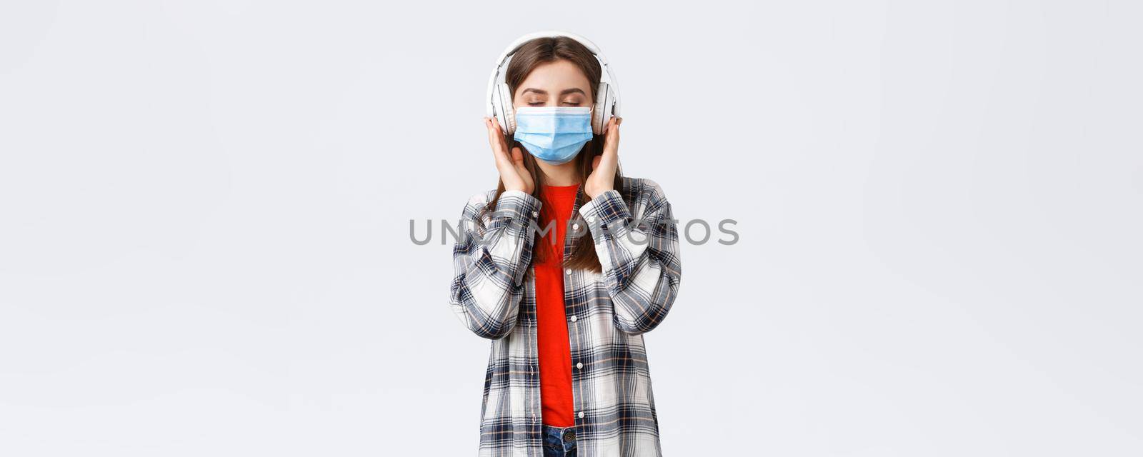 Social distancing, leisure and lifestyle on covid-19, coronavirus concept. Carefree relaxed woman in medical mask carried away with music in headphones, close eyes from satisfaction nice sound.