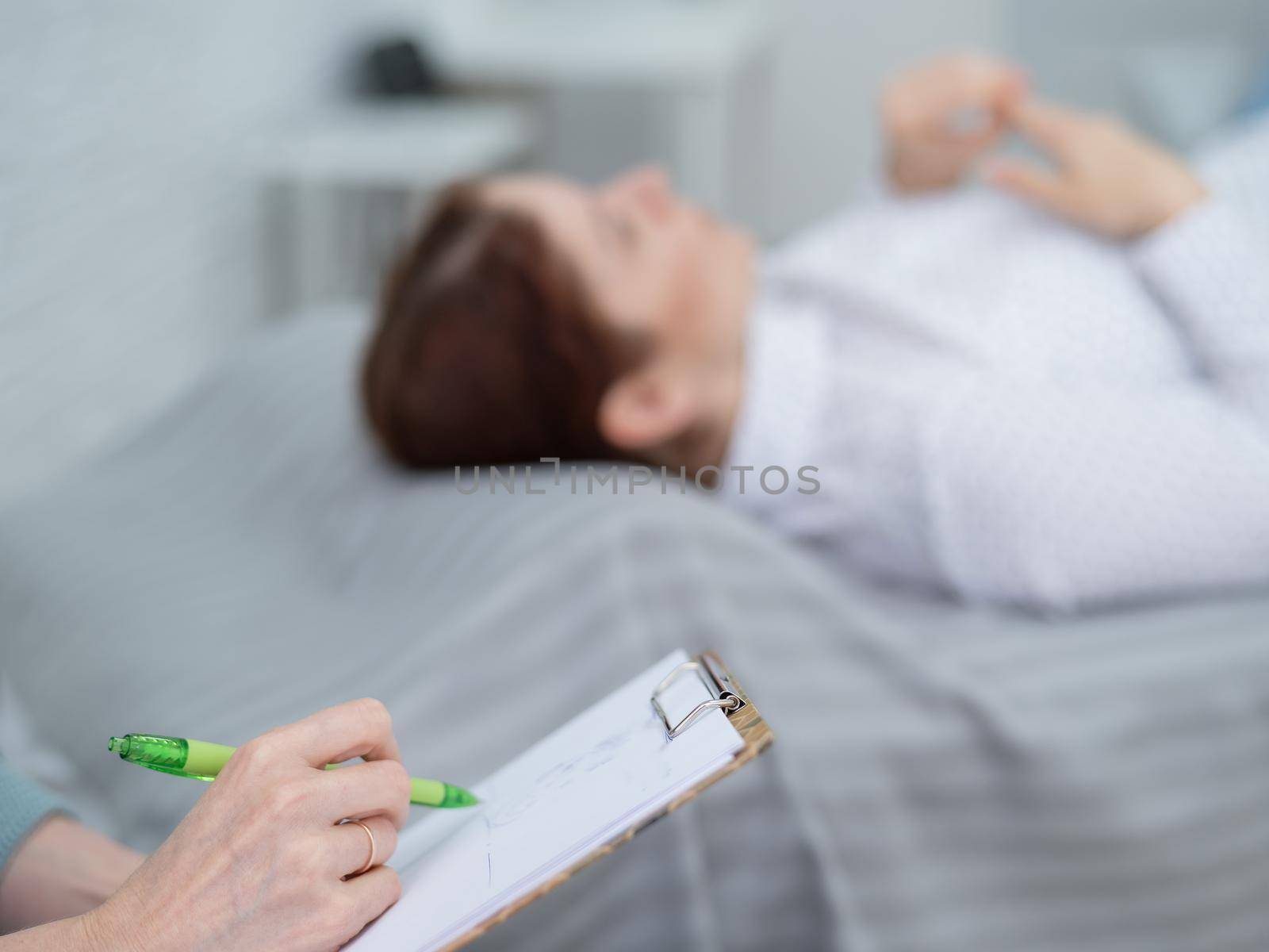 A caucasian woman lies on a couch and expresses her feelings, while a psychologist makes notes on a tablet