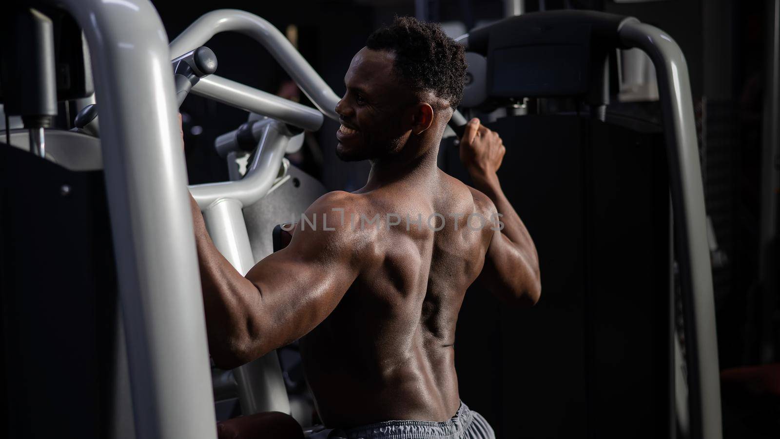 Shirtless african american man doing back exercises on a machine in the gym