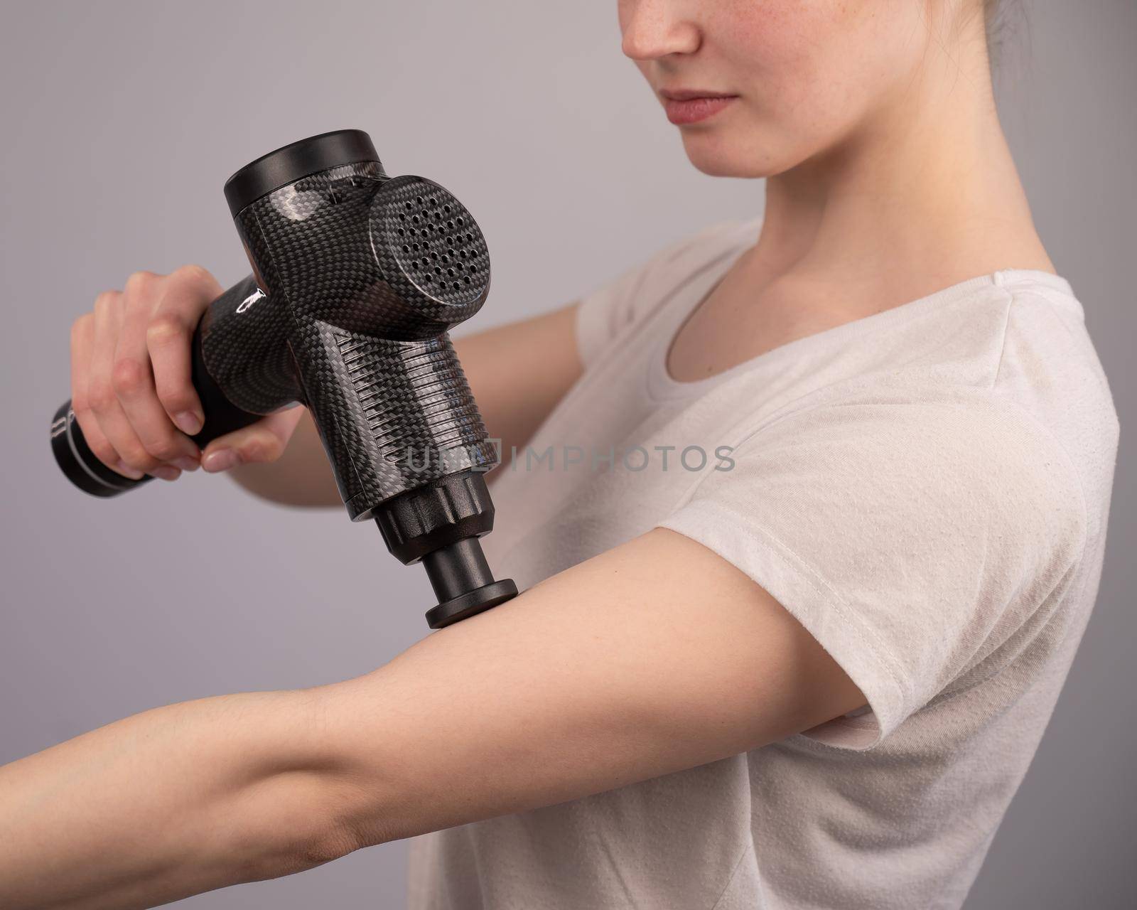 Caucasian woman uses a massager gun for pain in the muscles of the arm