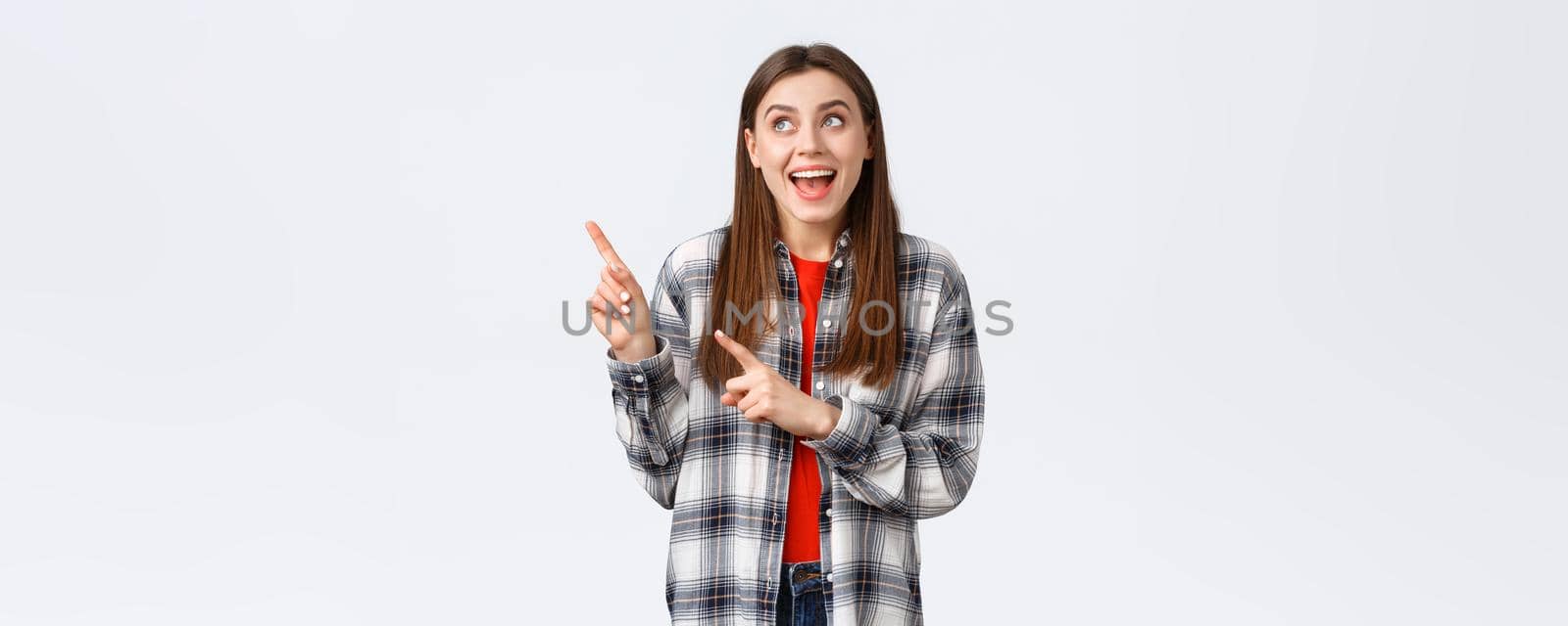 Lifestyle, different emotions, leisure activities concept. Excited happy woman in checked shirt pointing fingers upper left corner and smiling amused, making choice, found what she look for.