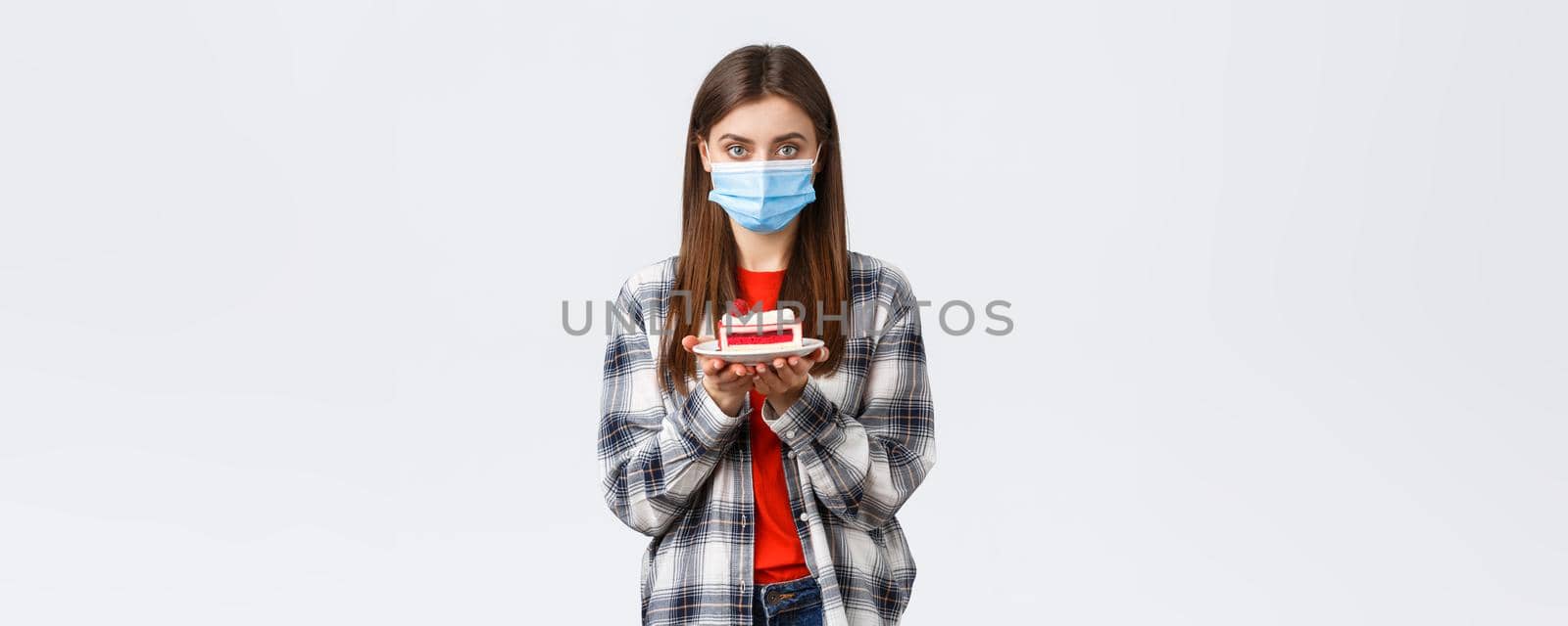 Coronavirus outbreak, lifestyle during social distancing and holidays celebration concept. Young cute girl in medical mask and casual outfit, holding birthday cake and looking serious camera.
