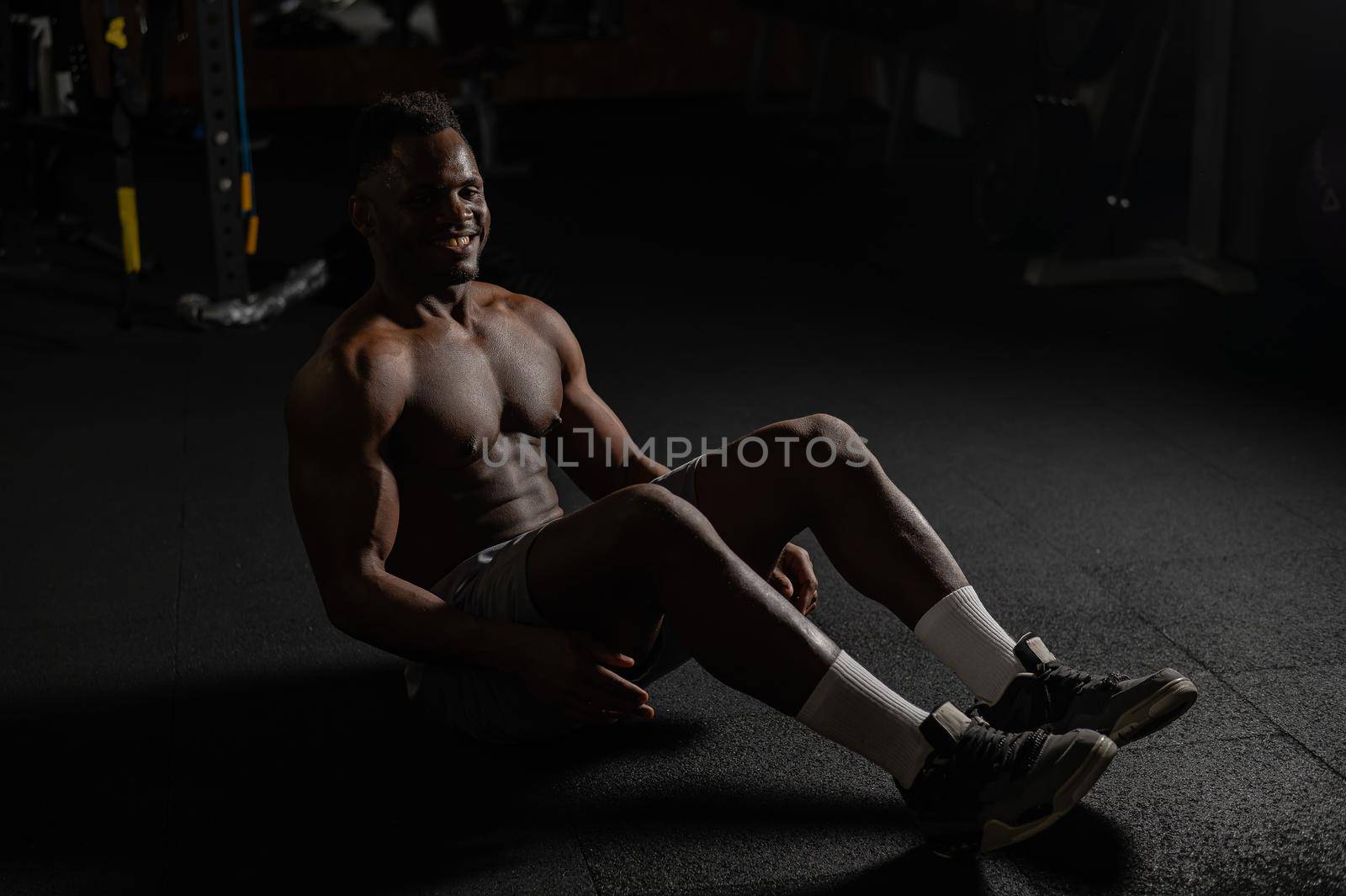 Afro american man doing abdominal exercises in a dark studio. by mrwed54