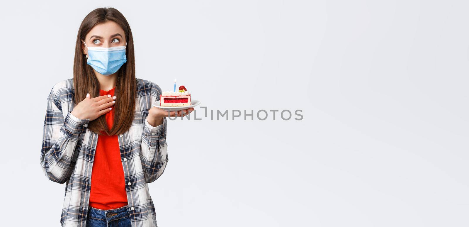 Coronavirus outbreak, lifestyle during social distancing and holidays celebration concept. Dreamy attractive woman in medical mask making wish as holding birthday cake, look away imaging.