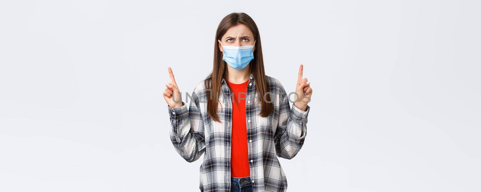 Coronavirus outbreak, leisure on quarantine, social distancing and emotions concept. Confused and doubtful young woman looking and pointing up with suspicious, disbelief face.