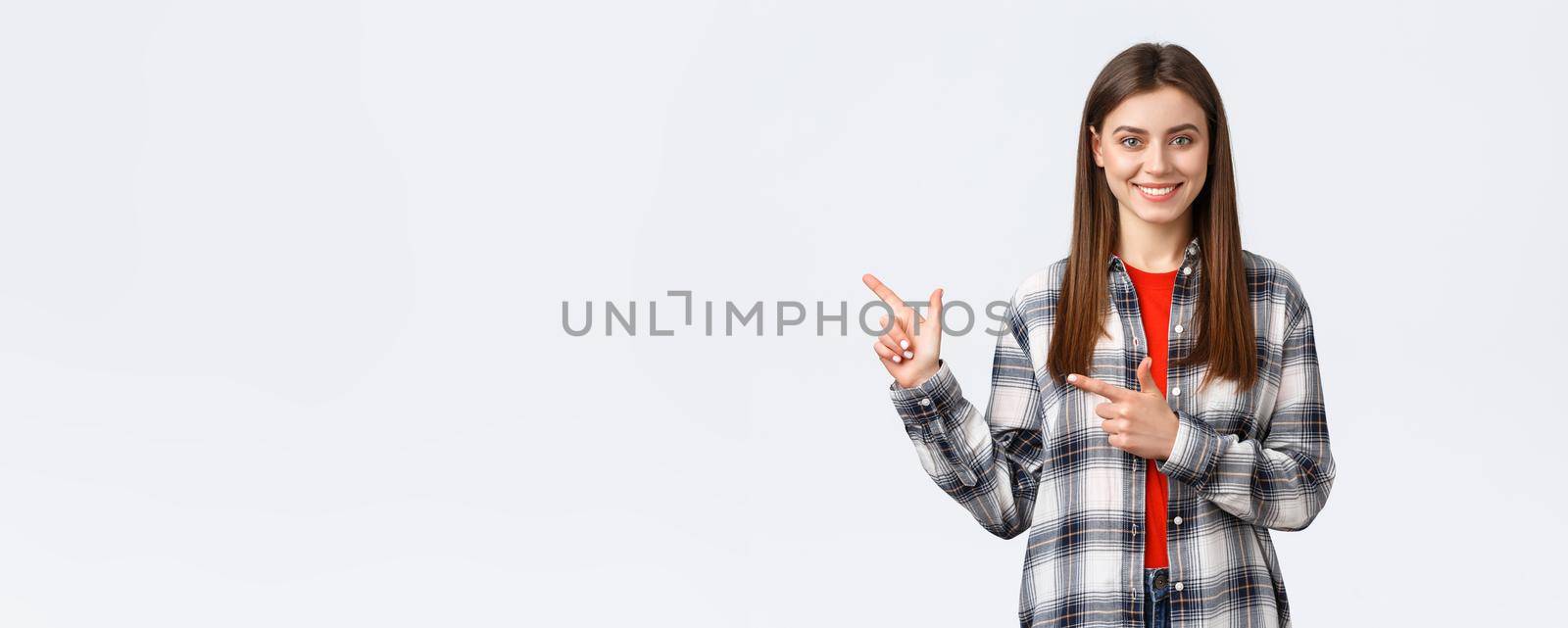 Lifestyle, different emotions, leisure activities concept. Pleasant smiling brunette girl in checked shirt, pointing fingers left, showing way to promo, recommend click link or buy product by Benzoix