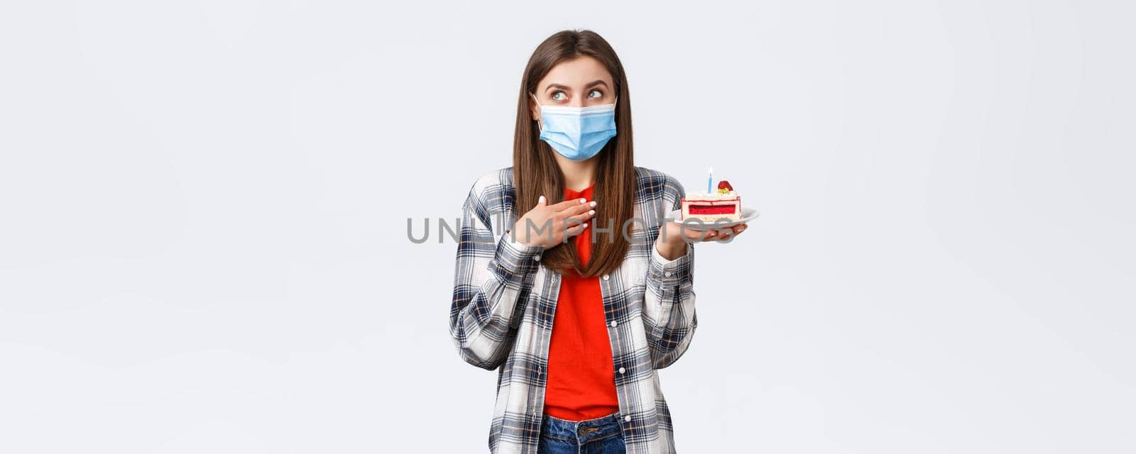 Coronavirus outbreak, lifestyle during social distancing and holidays celebration concept. Dreamy attractive woman in medical mask making wish as holding birthday cake, look away imaging by Benzoix