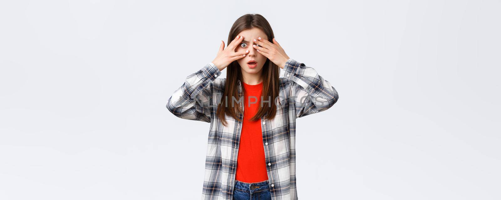 Lifestyle, different emotions, leisure activities concept. Shocked and speechless young pretty female in checked shirt, cover eyes from cringy thing but peeking through fingers.