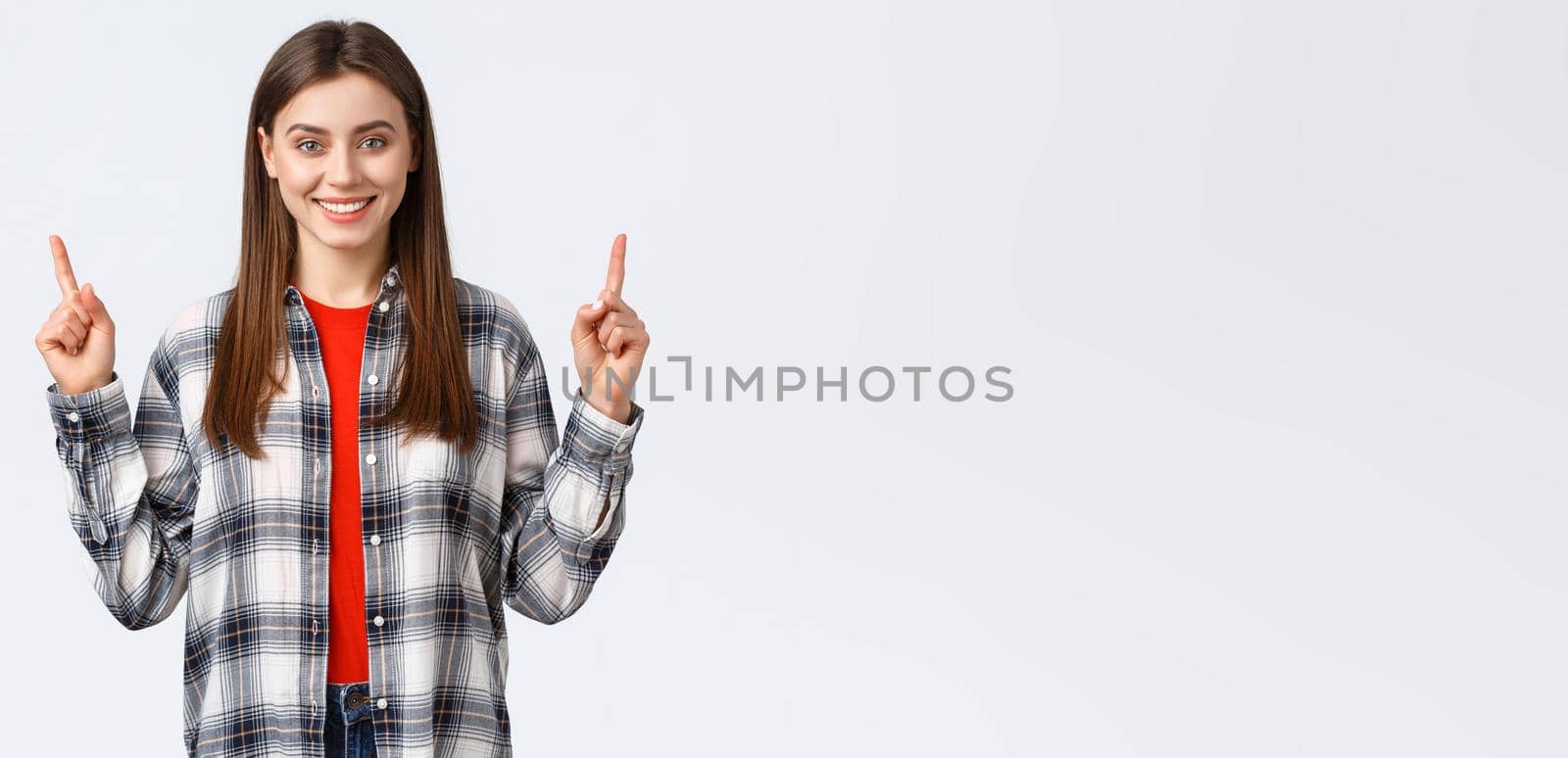 Lifestyle, different emotions, leisure activities concept. Confident smiling girl in checked shirt, turn attention to upper banner, pointing fingers up and look camera, telling about advertisement.