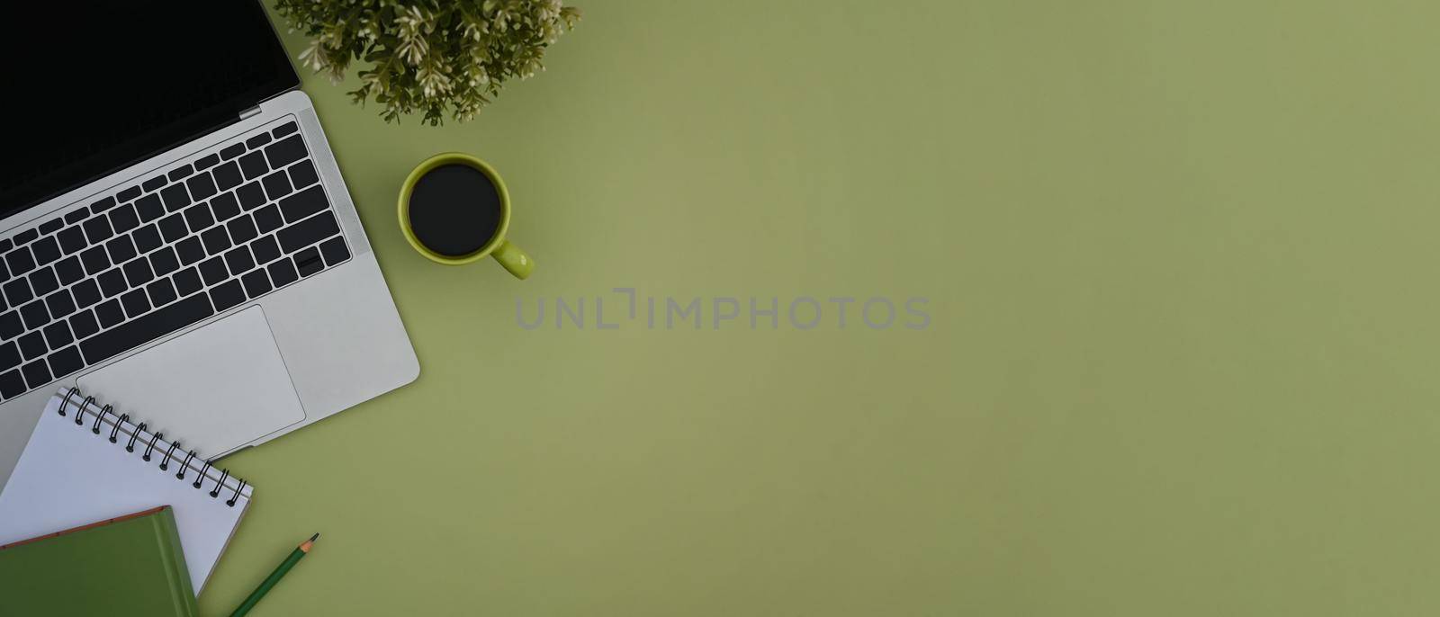 Top view laptop, notebook, coffee cup and potted plant on green background with copy space. by prathanchorruangsak