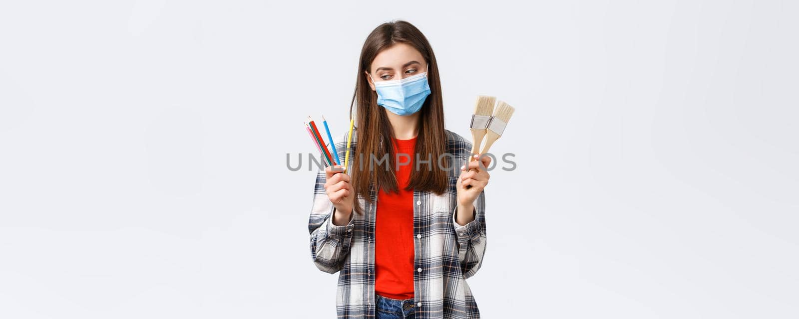 Social distancing, leisure and hobbies on covid-19 outbreak, coronavirus concept. Pleased smiling girl in medical mask start draw, look at colored pencils, show painting brushes by Benzoix