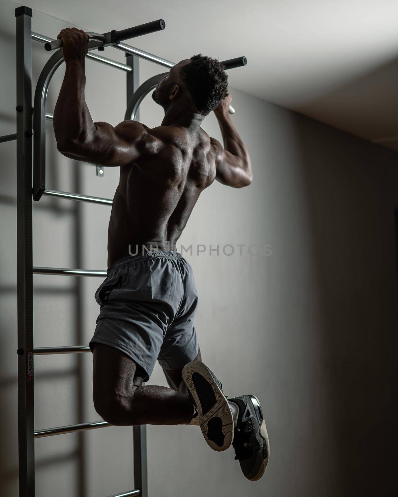 African american man with naked torso pulls up on horizontal bar in gym. by mrwed54