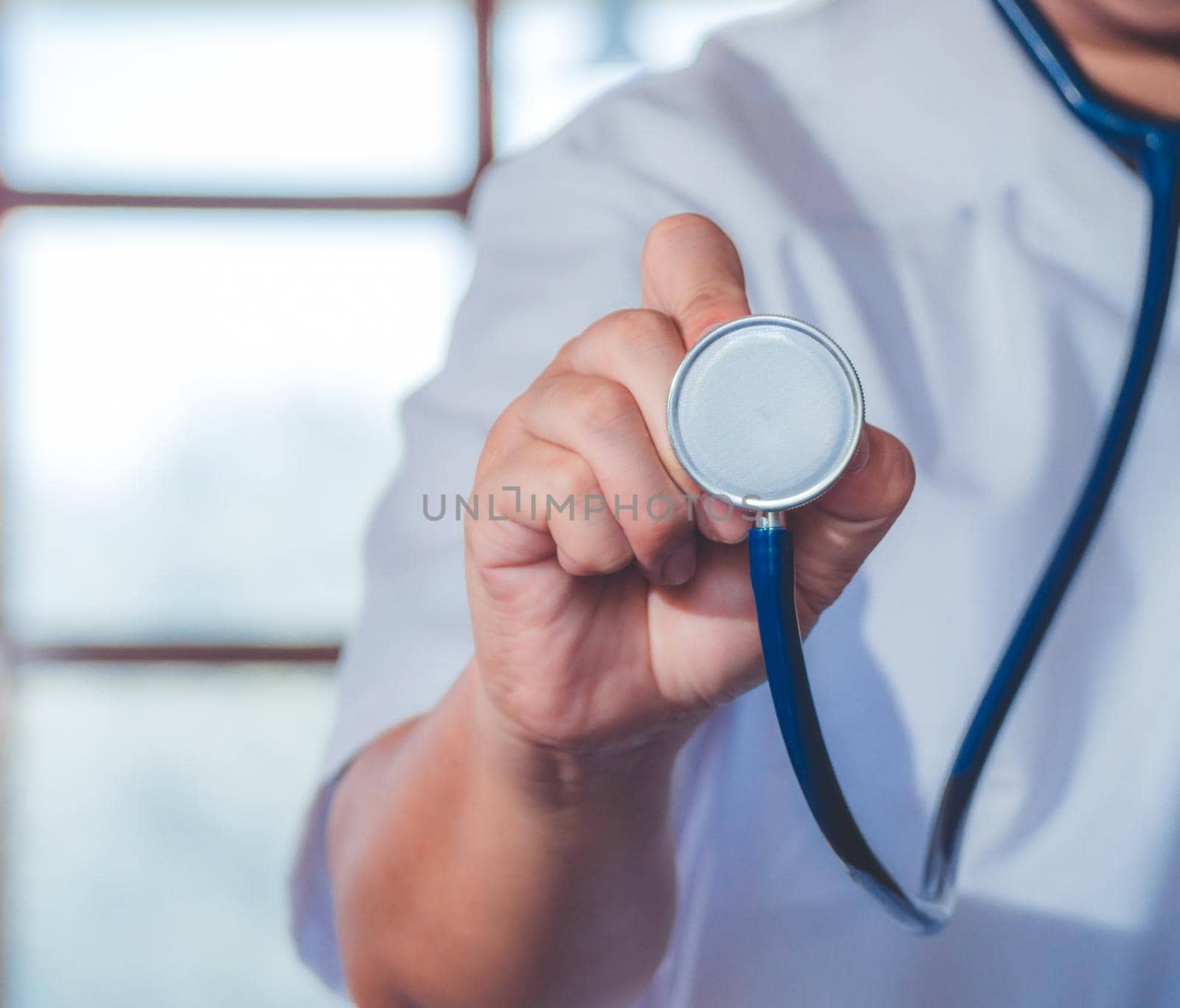 Male medicine doctor hand holding stethoscope against of chest on hospital background. Physician ready to examine patient. Medical and patient care concept. by Chakreeyarut