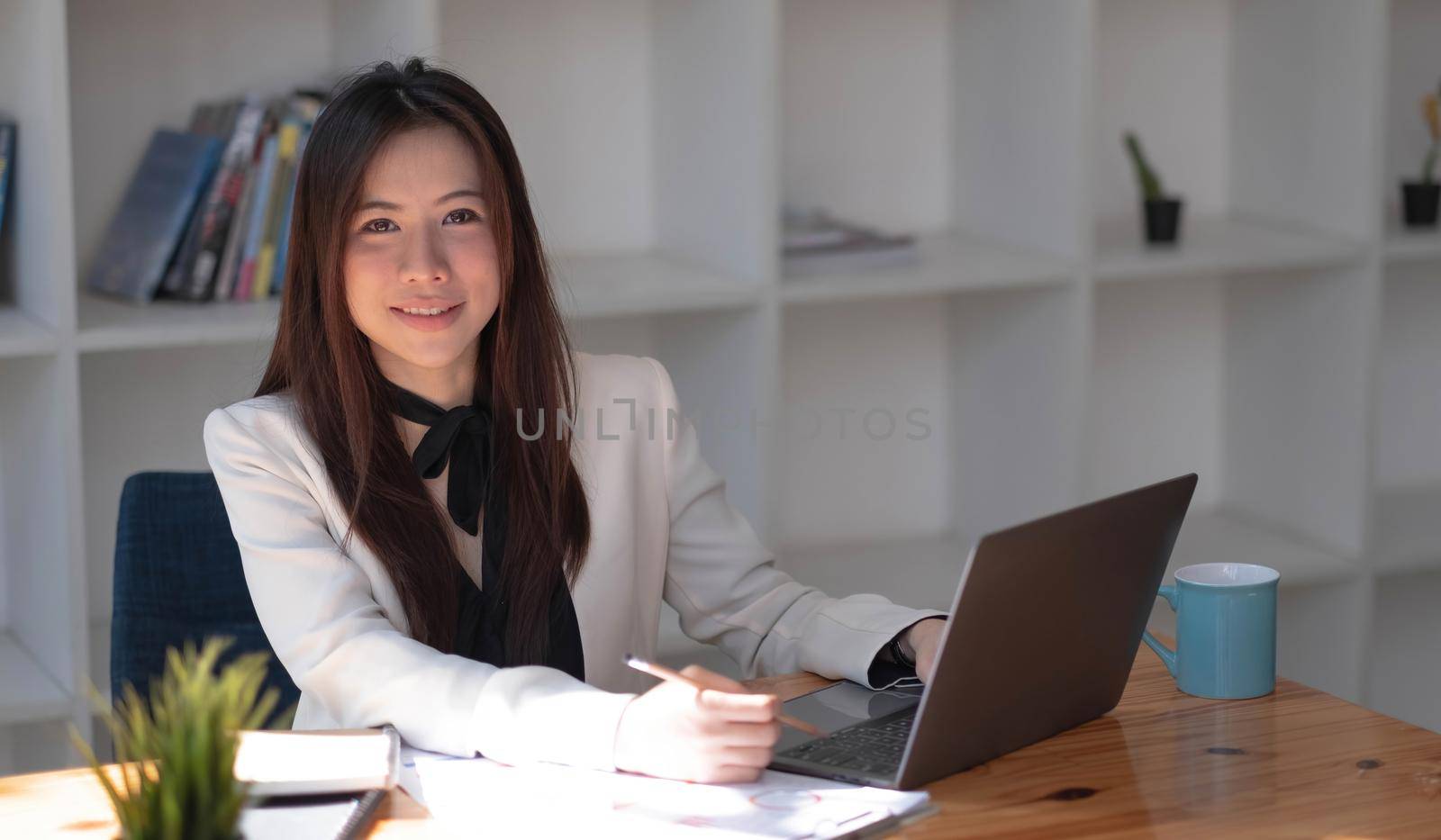 Charming Asian woman working at the office using a laptop Looking at the camera. by wichayada