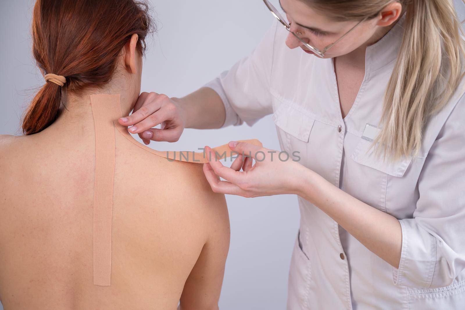 Female doctor glues kinesio tapes on the patient's shoulder