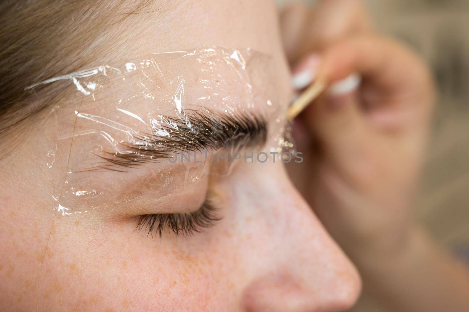 The master applies the composition for laminating the eyebrows to the client with a wooden spatula. by mrwed54