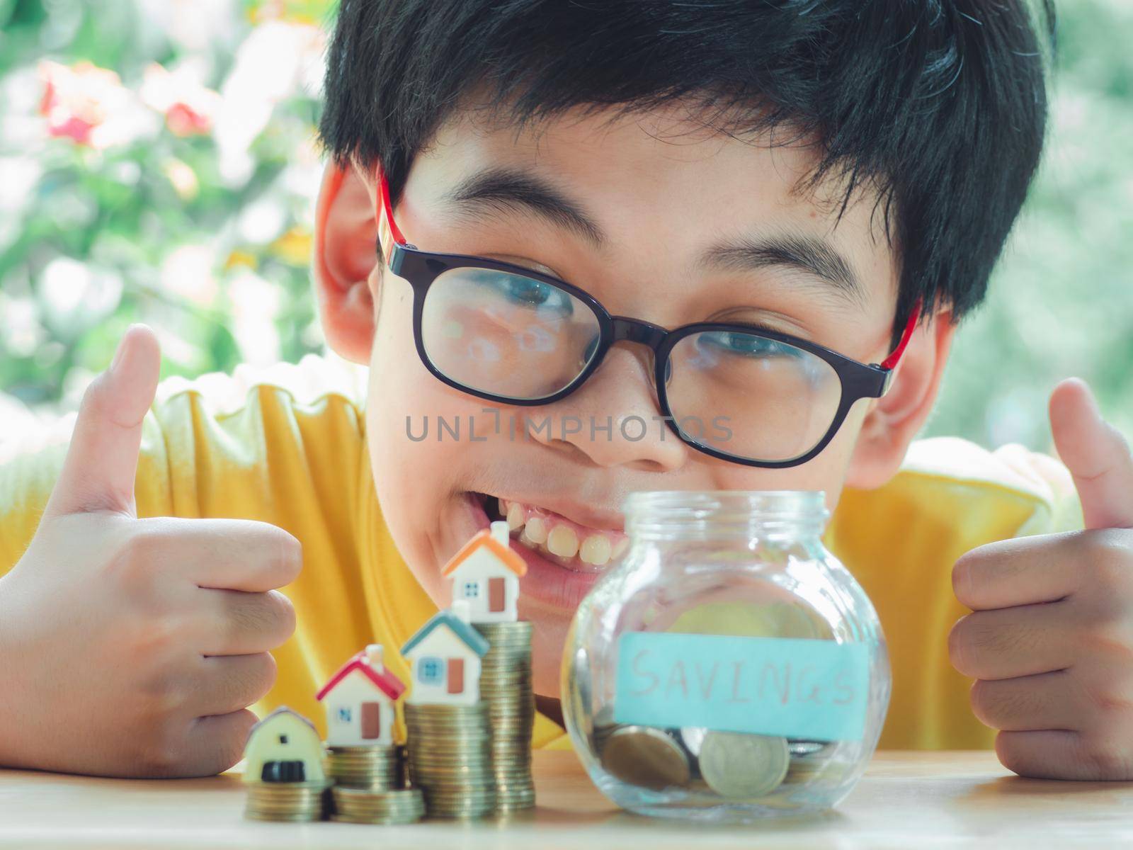 Asian boy holding coins drop a container saving money to save money invest for future and buy home.Concept loan, property ladder, financial, real estate investment and bonus. by Chakreeyarut