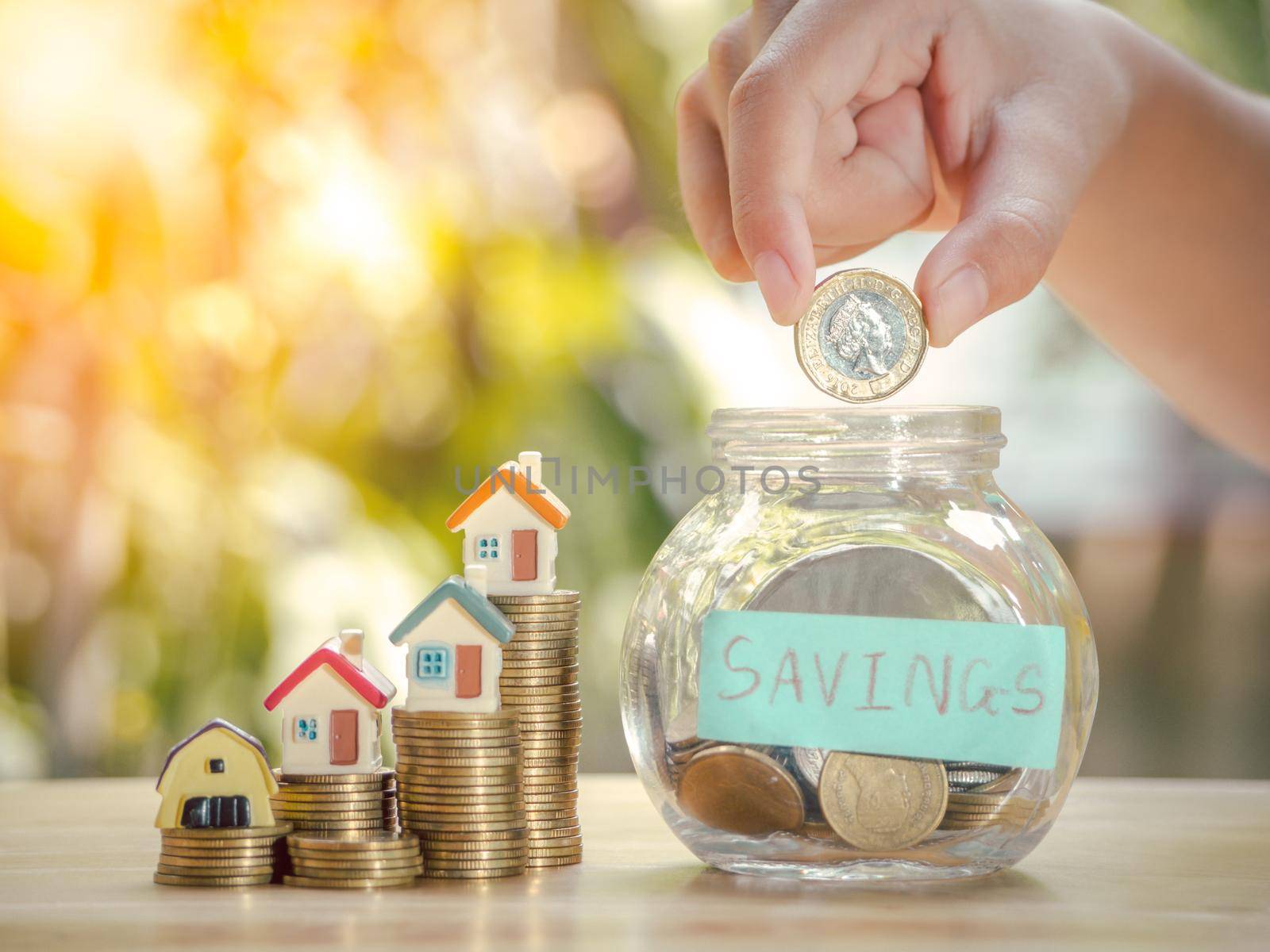 Asian boy holding coins drop a container saving money near home on gold coins stack to save money invest for future and buy home.Concept loan,property ladder,financial, real estate investment, bonus. by Chakreeyarut