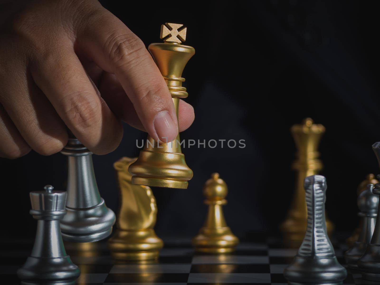 Hand of businessman holding gold king checkmate silver king on chess board to successfully in the competition. Management or leadership strategy and teamwork concept. by Chakreeyarut