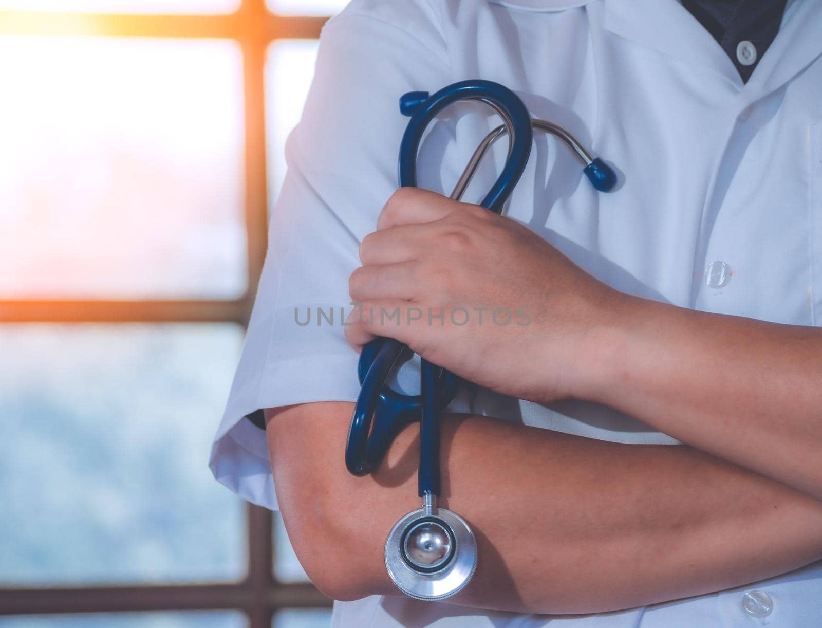 Male Doctor With Arms Crossed Holding Stethoscope in hospital. Healthcare and medicine concept. by Chakreeyarut