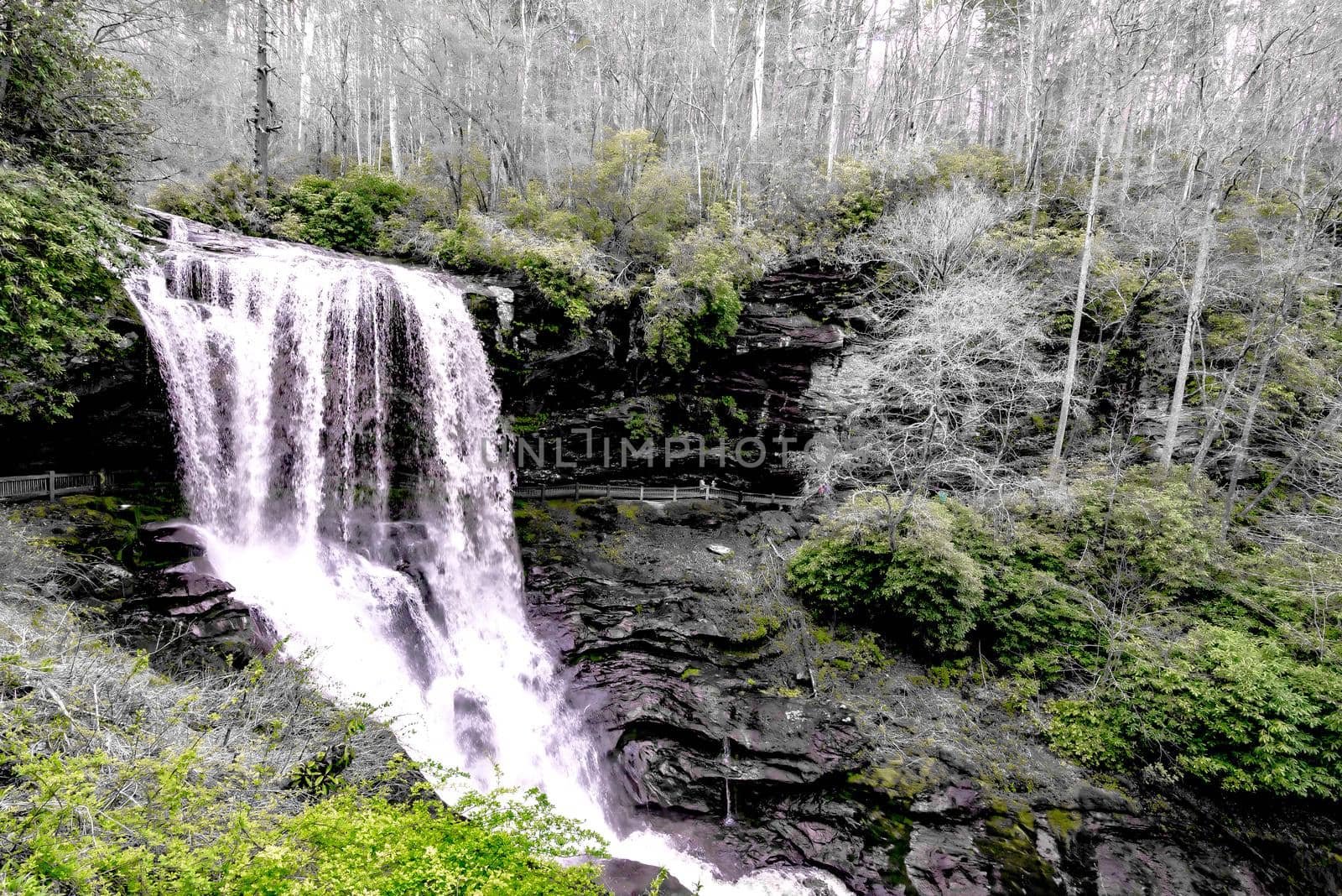 A scenic waterfall roadside going over the cliff down to the boulders and rocks below where you can no longer drive under but can walk underneath the raging waters by digidreamgrafix