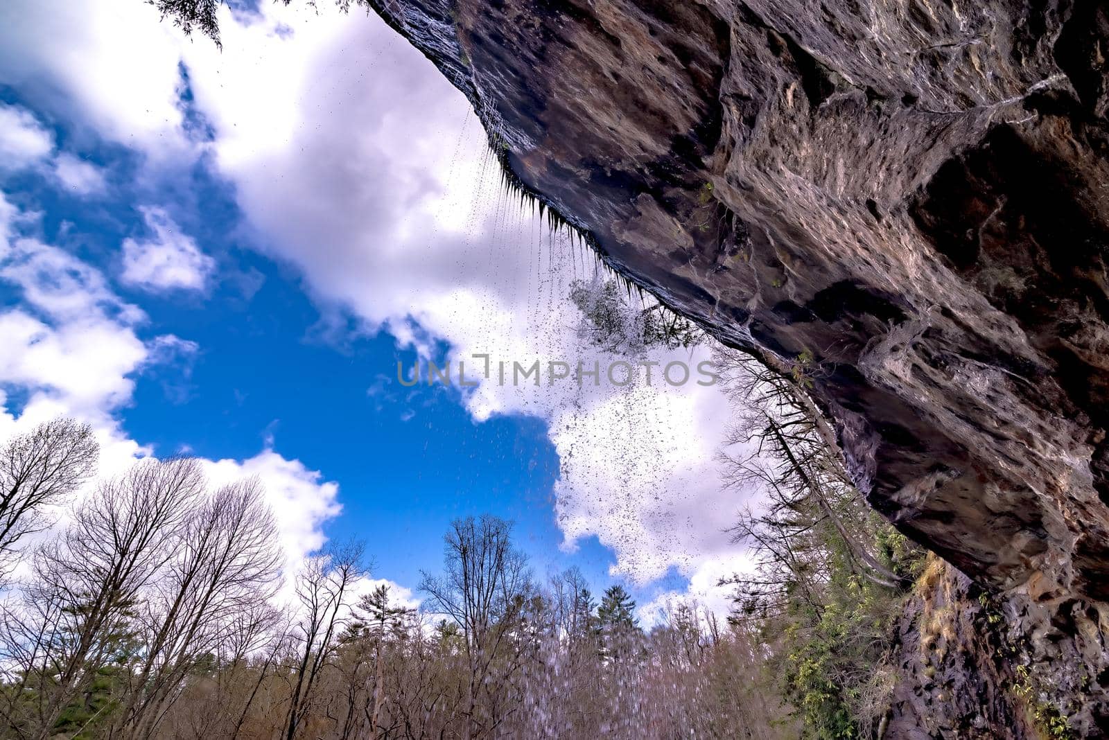 A scenic waterfall roadside going over the cliff down to the boulders and rocks below where you can no longer drive under but can walk underneath the raging waters by digidreamgrafix