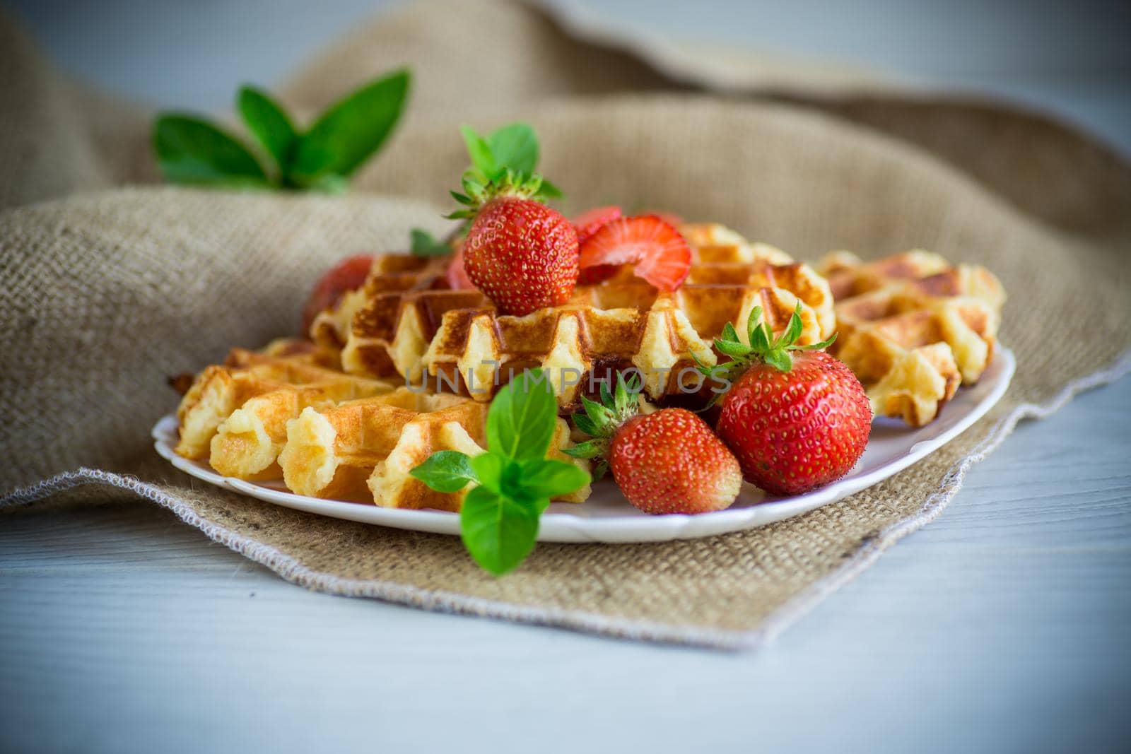 Sweet curd cooked waffles with fresh ripe strawberries, on a wooden table.