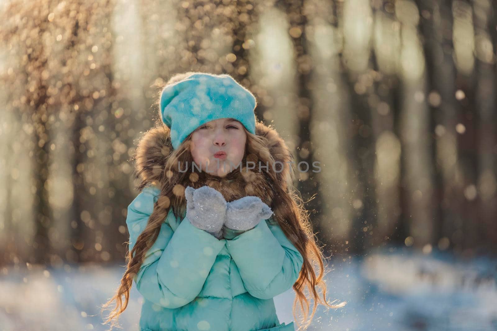 little girl blows on the snow that is on her mittens