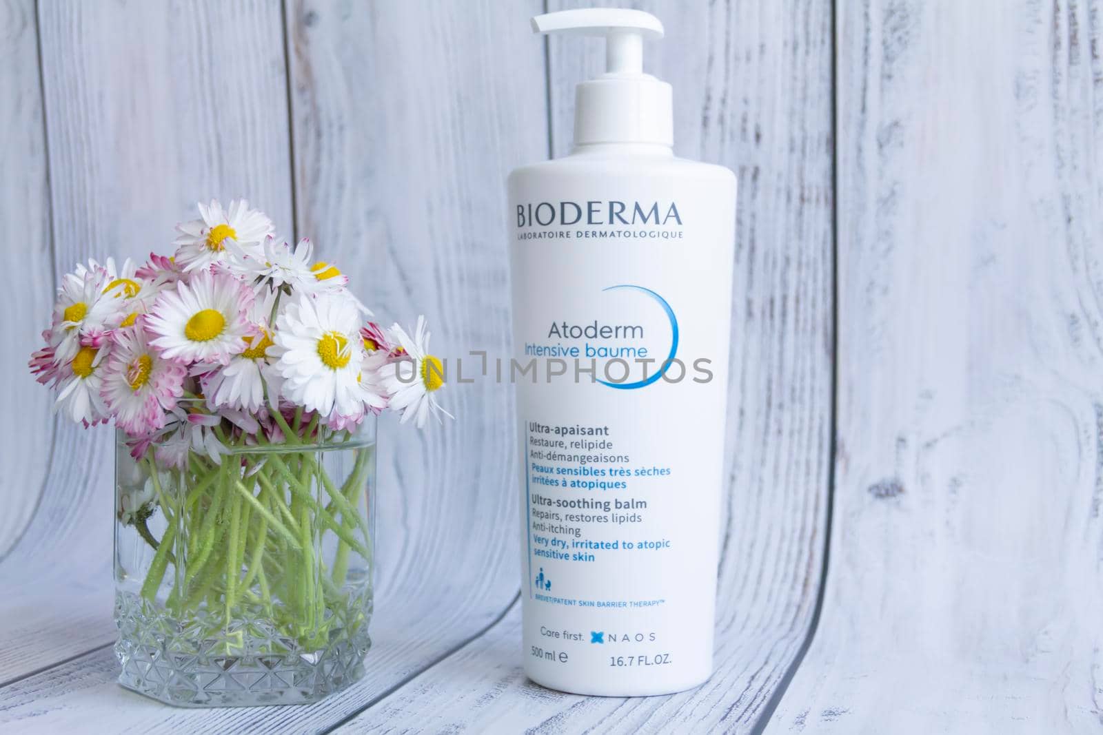 Bioderma dry skin care balm with a bouquet of white daisies on a wooden background. Cosmetic products.