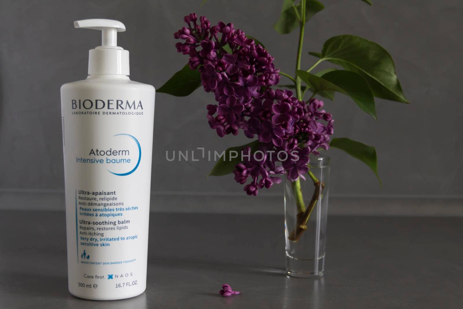 Bioderma dry skin care balm with a bouquet of purple lilac on a wooden background. Cosmetic products.