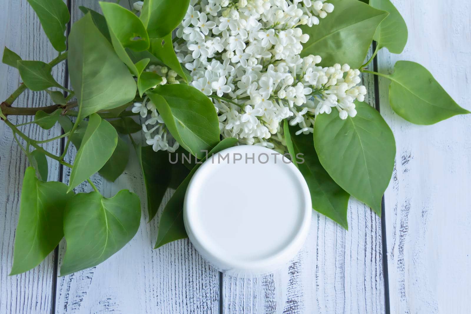 One white box with cosmetic products and creams with fresh, blooming and fragrant lilac flowers and free space for advertising.