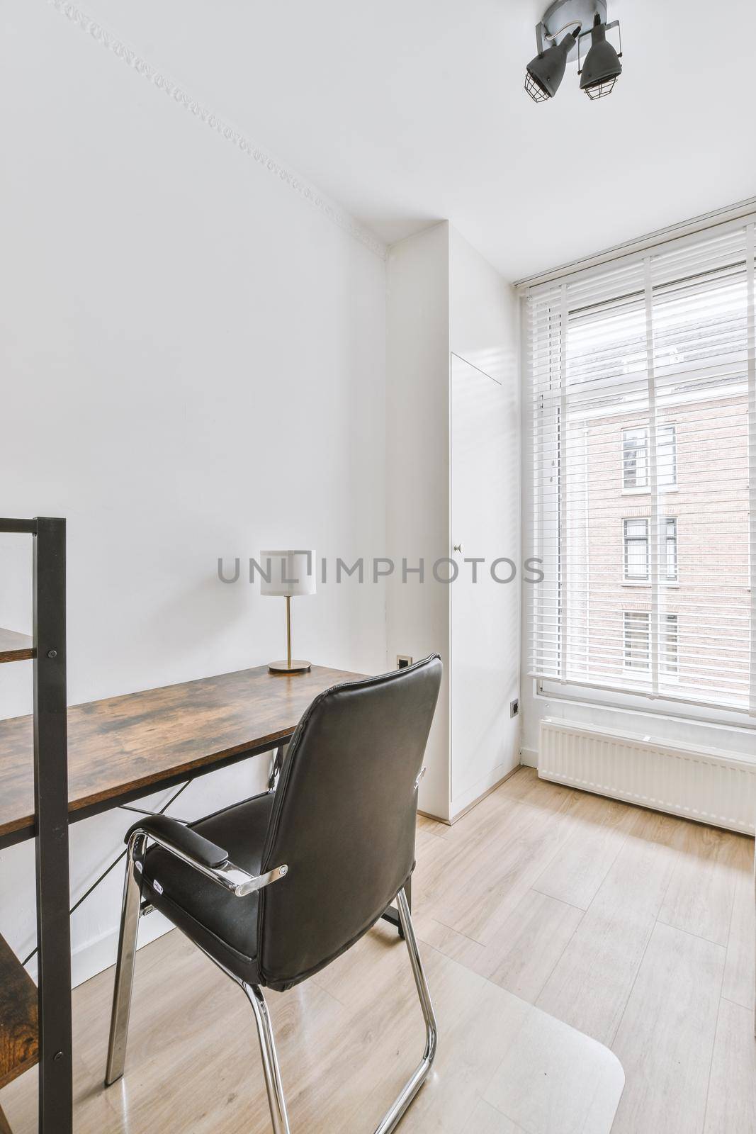 Minimalist interior of study room with parquet floor and white walls furnished with settee and table with shelf rack