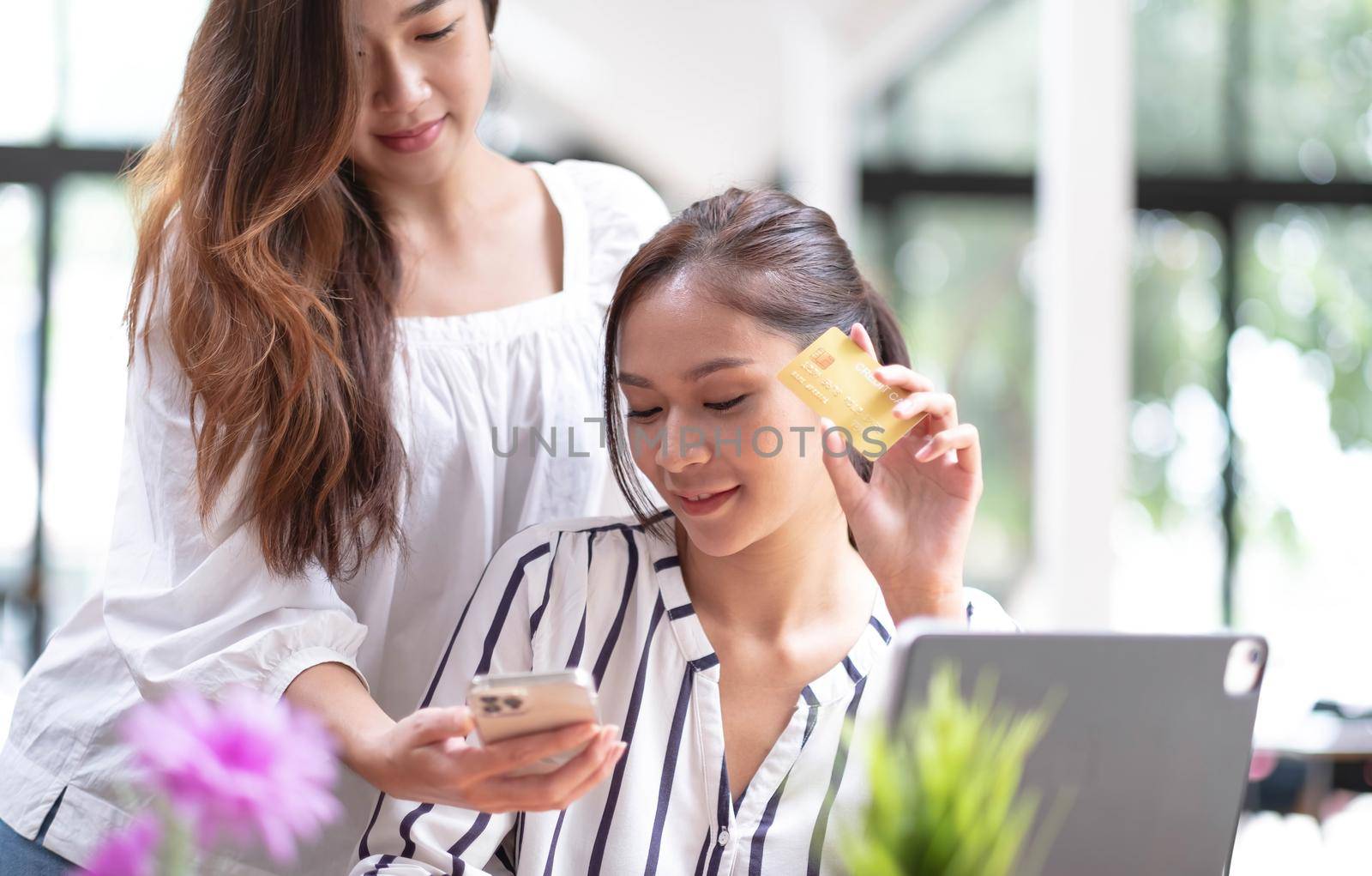 Asian two woman friend enjoy shopping online at cafe. Beautiful lesbian couple sit on sofa, holding credit card to make e bank online payment after use phone purchase goods in web store.