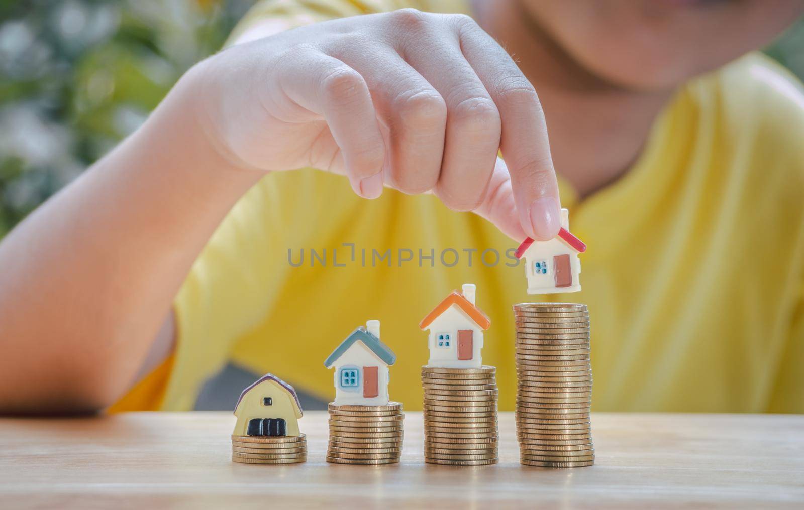 Asian boy holding home or house on gold coins stack to saving money invest for future and buy home.Concept loan, property ladder, financial, real estate investment and bonus.