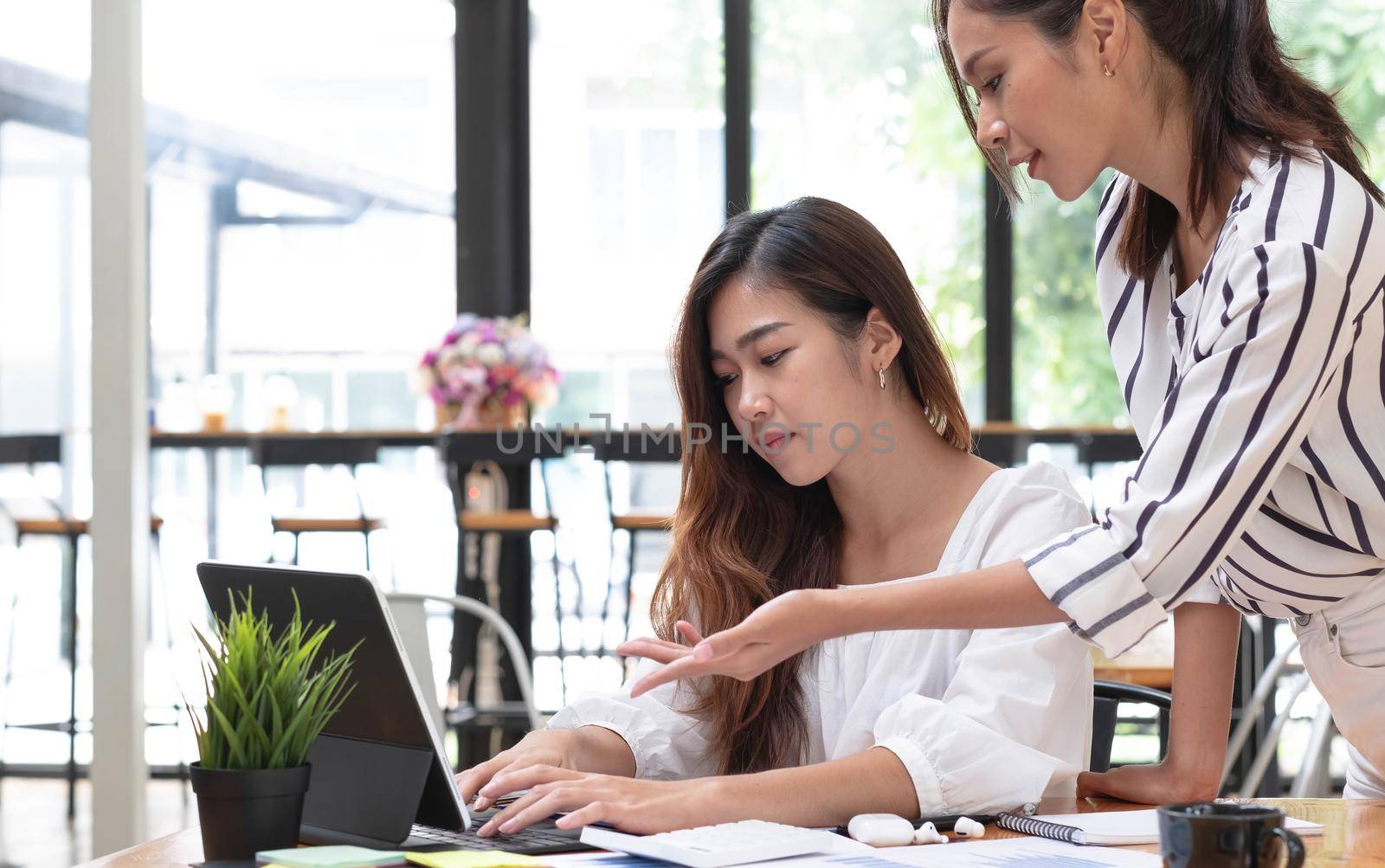 Two young beautiful asian business woman in the conversation, exchanging ideas at work..