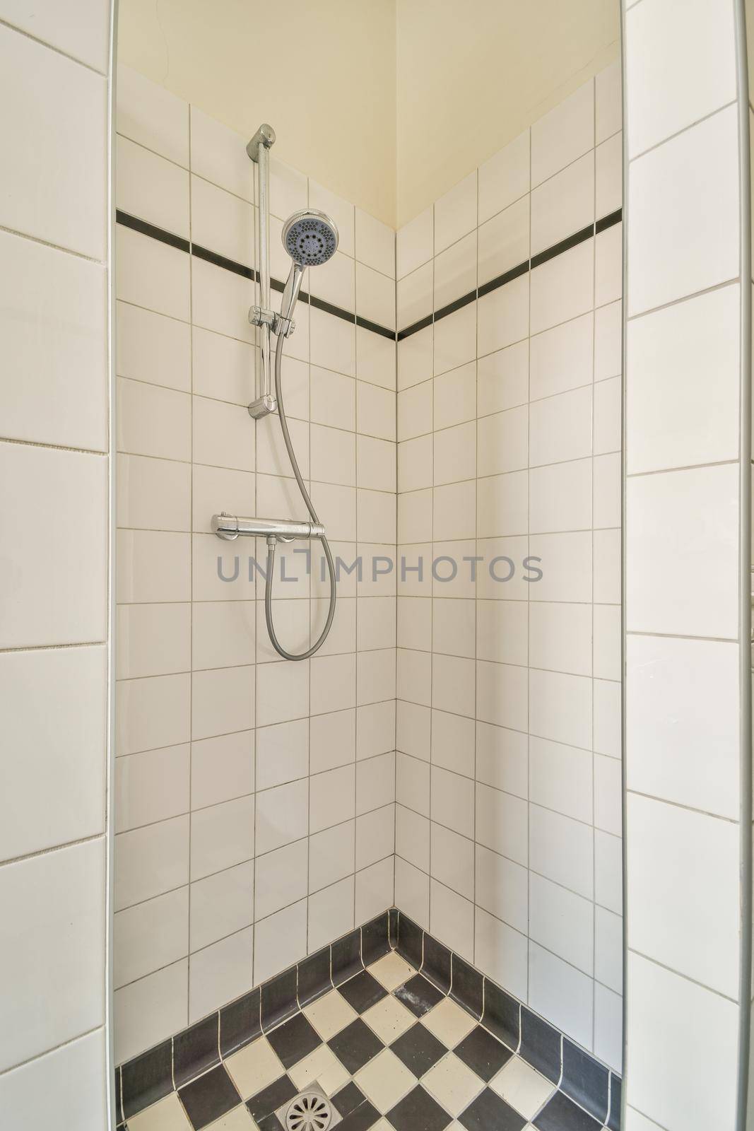 Shower faucets attached to tiled wall near glass partition and ornamental curtail in washroom at home