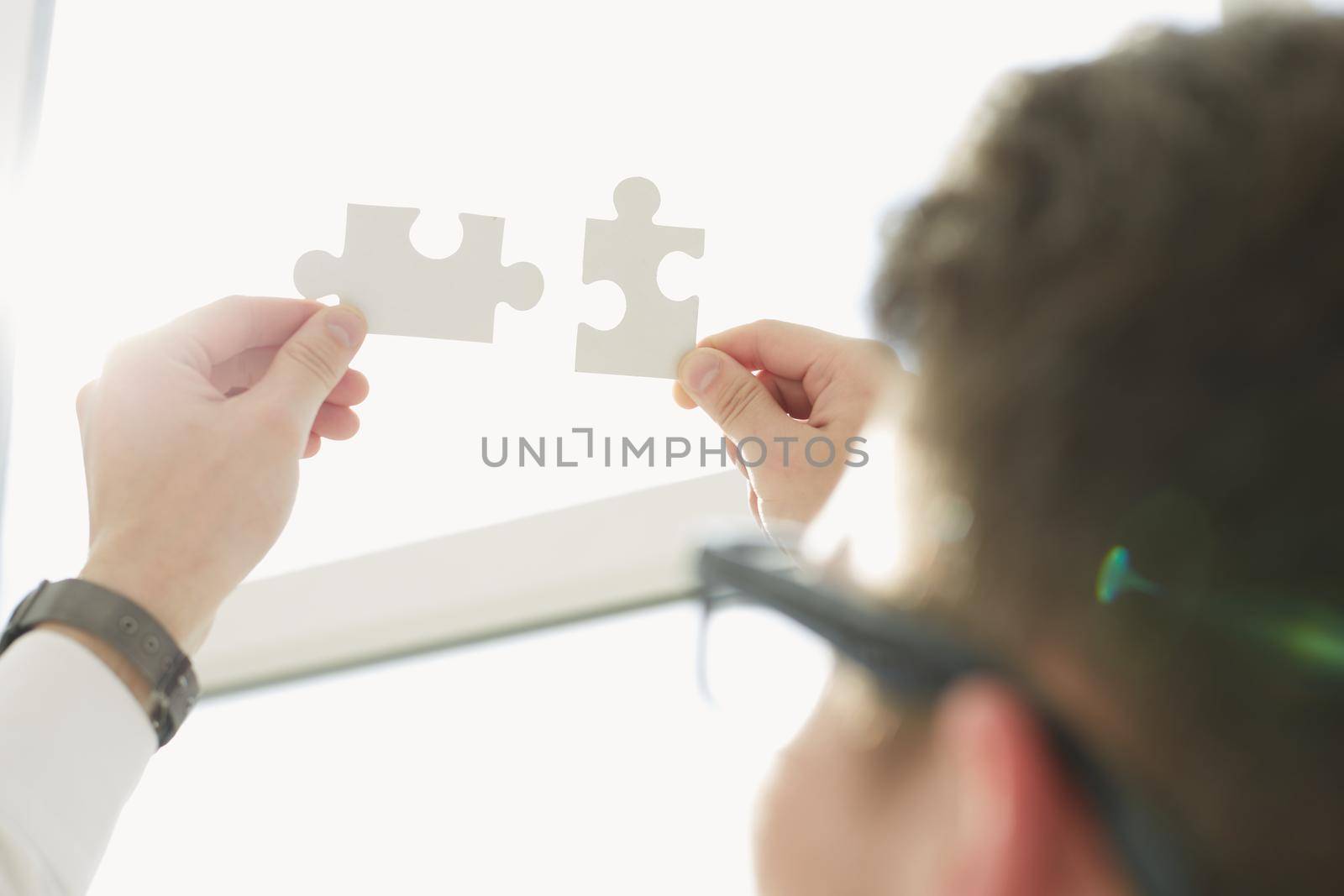 Businessman hands connecting puzzle pieces representing the merging of two companies or joint venture, partnership, Mergers and acquisition concept. by Prosto