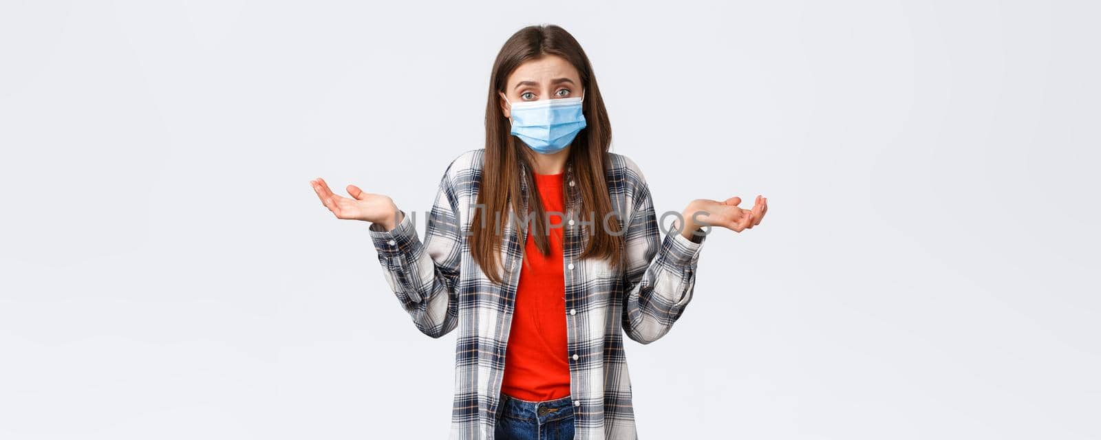 Coronavirus outbreak, leisure on quarantine, social distancing and emotions concept. Confused and indecisive young woman in medical mask dont know what do, shrugging with hands spread sideways.