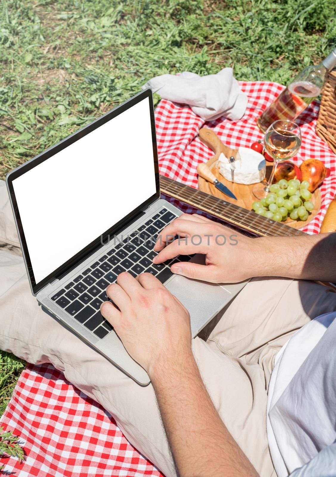 unrecognizable man in white pants outside having picnic and using laptop, working outdoors. summer leisure and fun