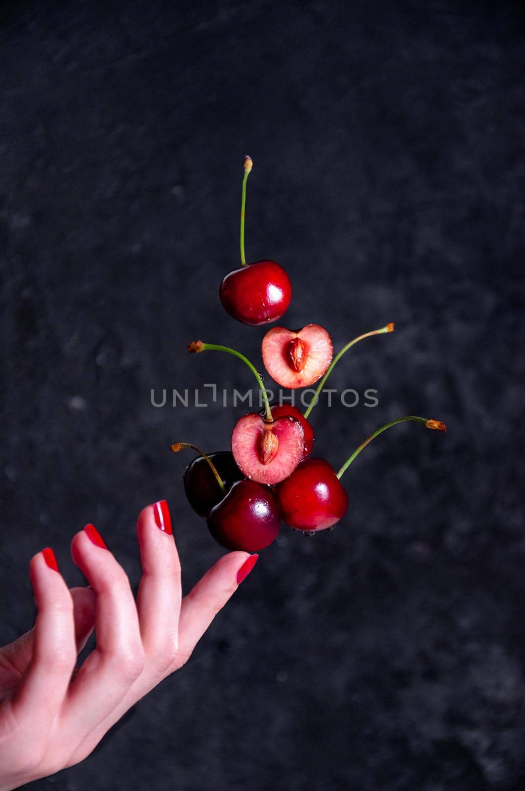 Close up Composition of Levitation Cherries on Woman Finger on the Dark Background.