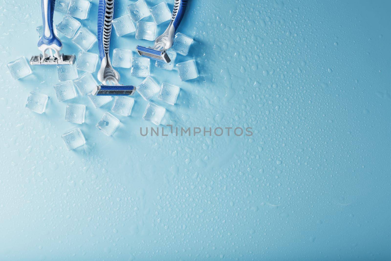 Blue shaving machines in a row on a blue background with ice cubes. The concept of cleanliness and frosty freshness