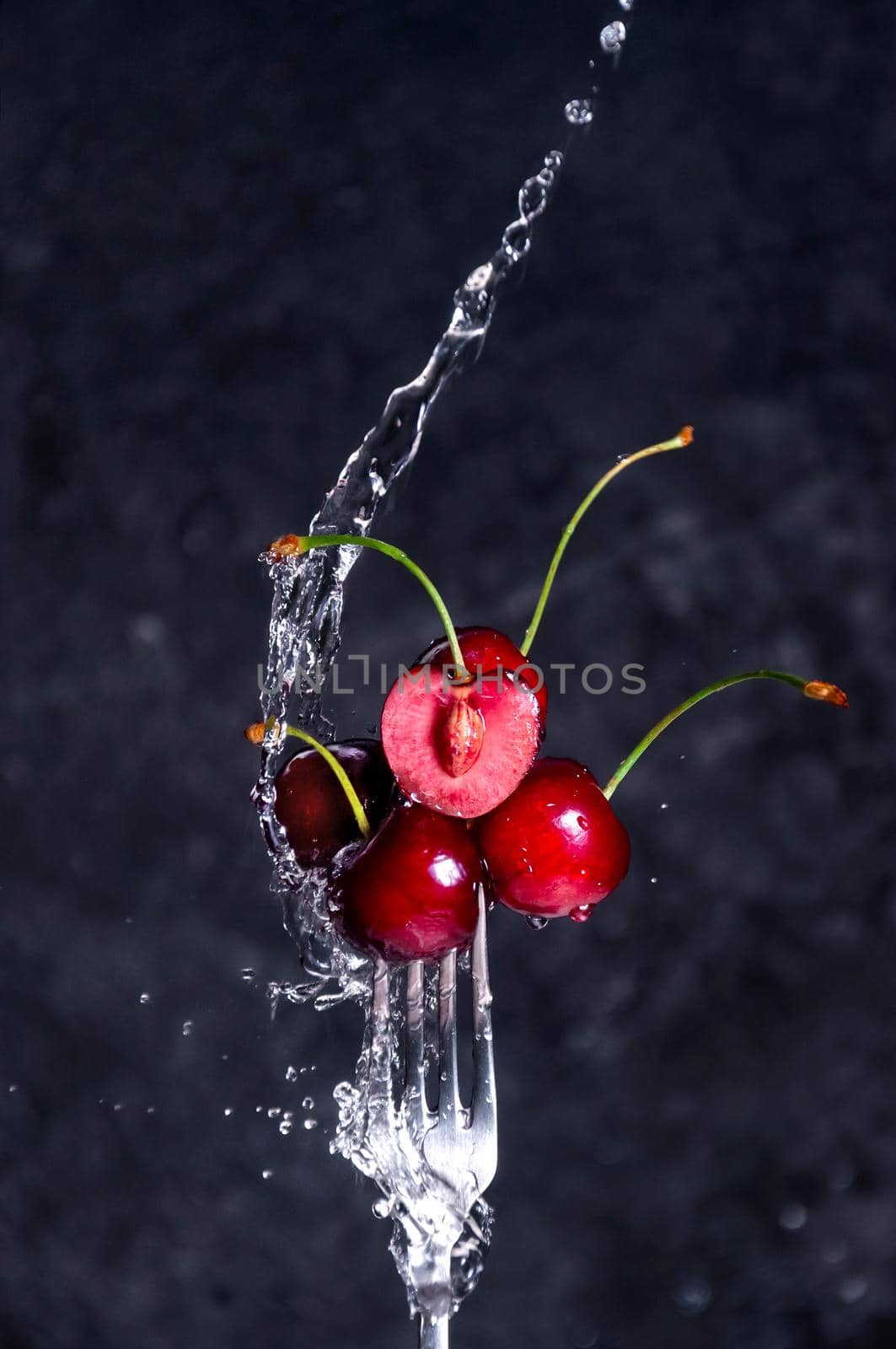 Close up Composition of Cherries on Fork Flying in the air with Water Splashes on the Dark Background.