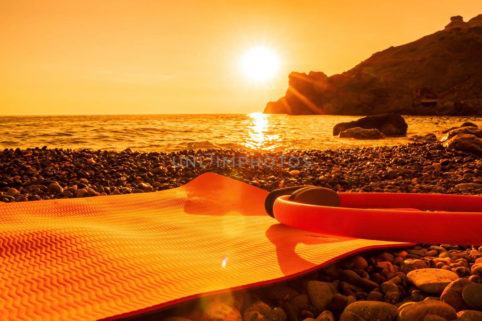 Young woman with long hair in white swimsuit and boho style braclets practicing outdoors on yoga mat by the sea on a sunset. Women's yoga fitness routine. Healthy lifestyle, harmony and meditation