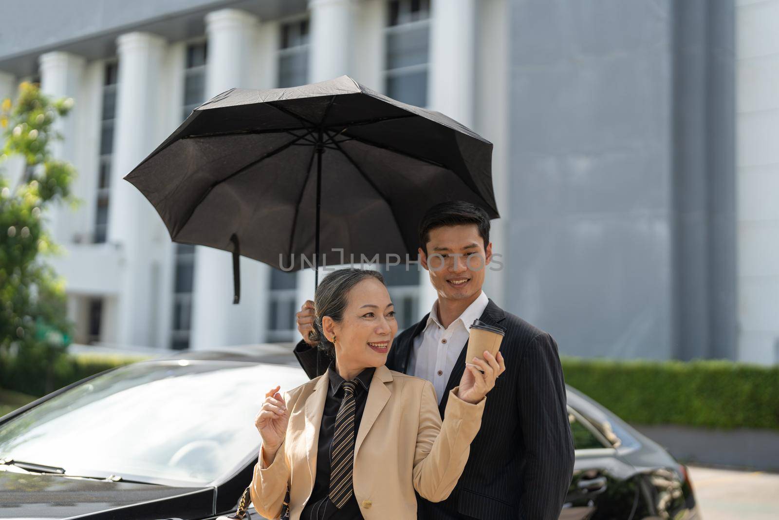 Happy senior old asian businesswoman discussion talking about new project with young asian male colleague at car park